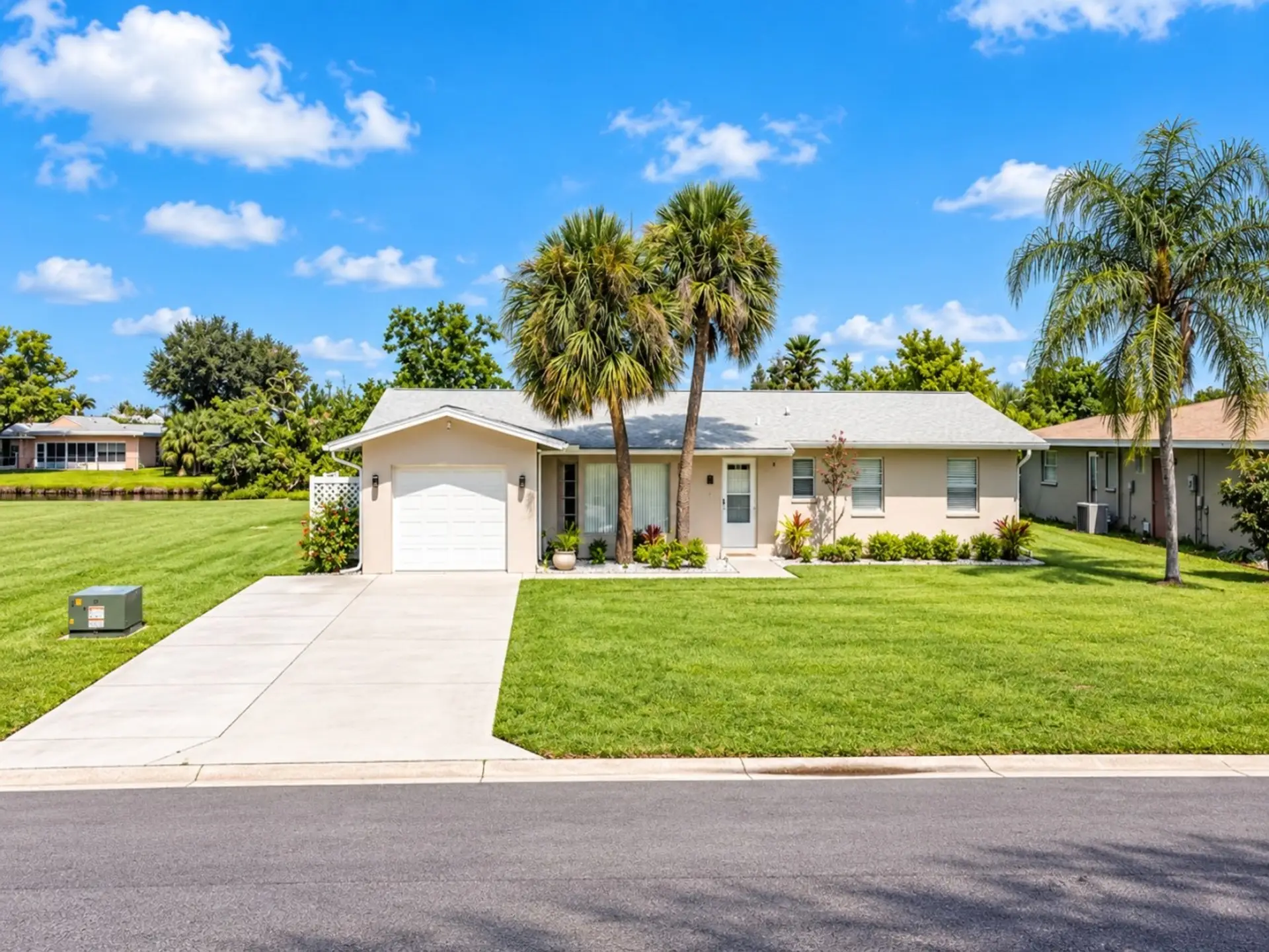 Bright Florida vacation home exterior at Sunkissed on Annapolis in Rotonda West, featuring palm trees, a spacious lawn, and convenient driveway parking.