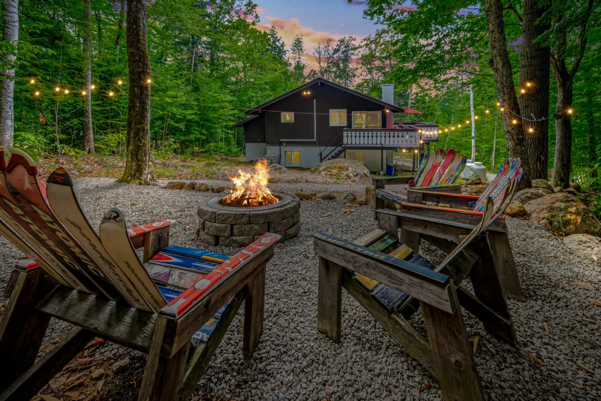 Peaceful backyard fire pit surrounded by Adirondack chairs, string lights, and forest views. Perfect for cozy nights, s’mores, and making memories with family and friends in the White Mountains.