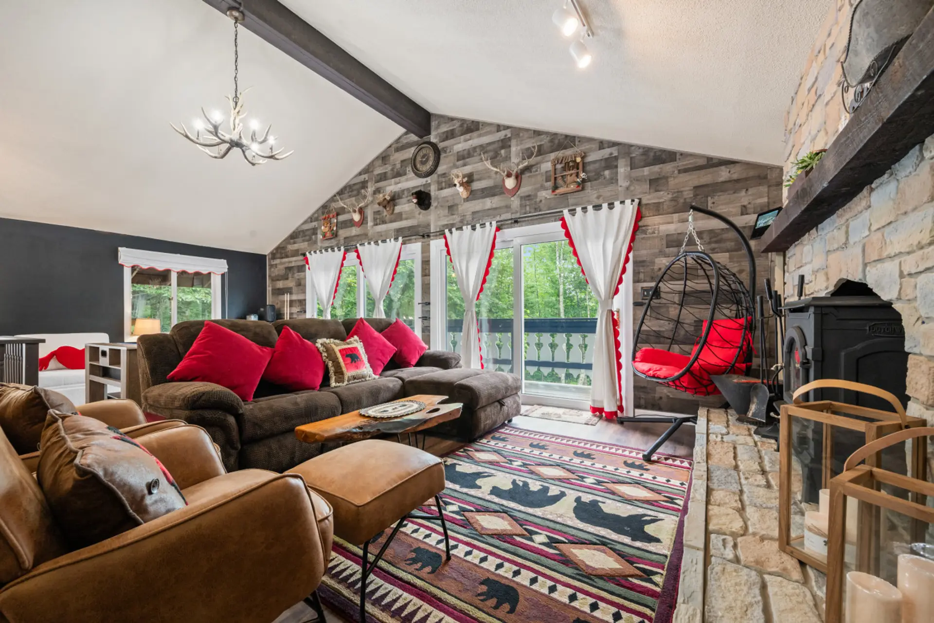 Family-friendly White Mountains chalet living room with wood stove, stone hearth, vaulted ceilings, mountain-inspired decor, swing chair, large sectional, smart TV area, and direct access to the outdoor deck.