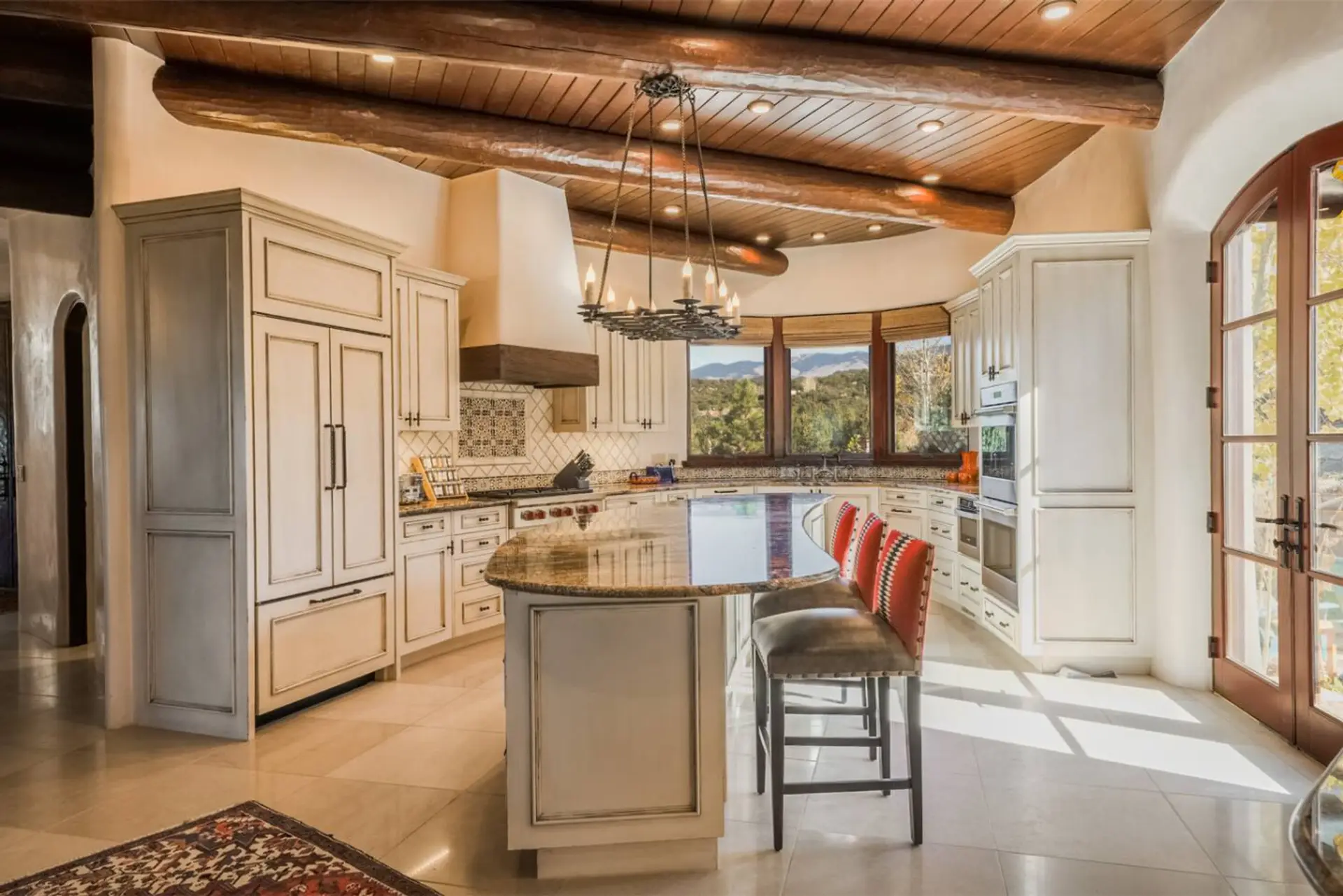 White washed finishes on the kitchen cabinetry compliment rustic tile, vigas and plaster on the walls for a stunning Santa Fe kitchen.