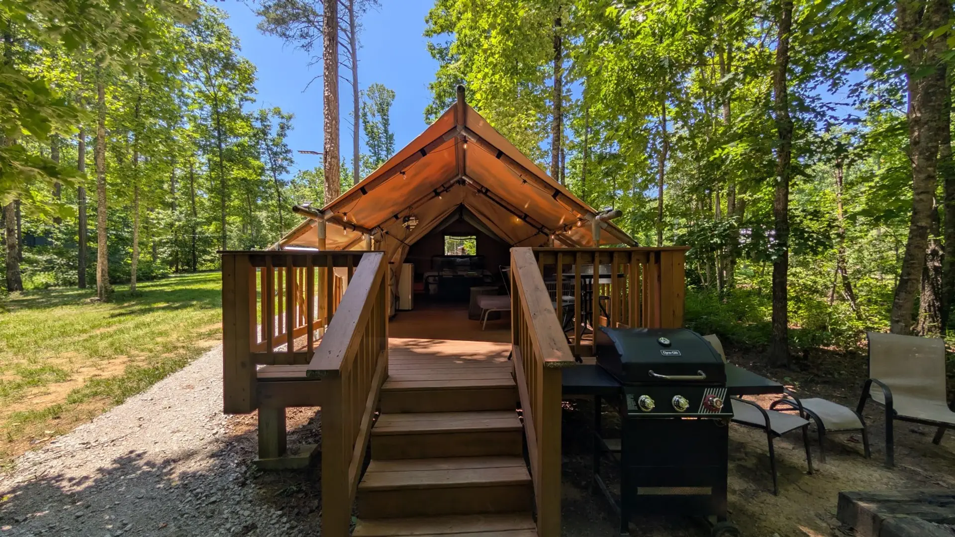 Stepping up to the Glamping Tent. Stairs lead through the open canvas straight to the bed at the back, with a propane grill on the right and the woods on all sides.