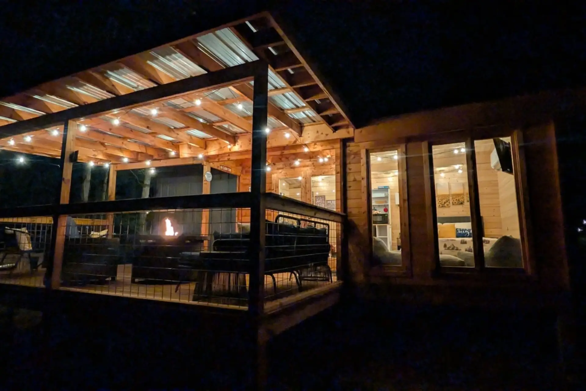 Same view at night, with the fire table glowing through the railings, the bedroom lit warm through the glass, and string lights overhead.