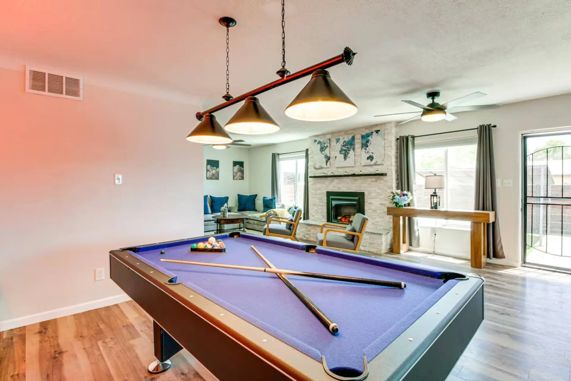 Full regulation pool table with blue felt, industrial pendant lights, and the gas fireplace glowing in the background. This is the game room that wins the group over before they even unpack.