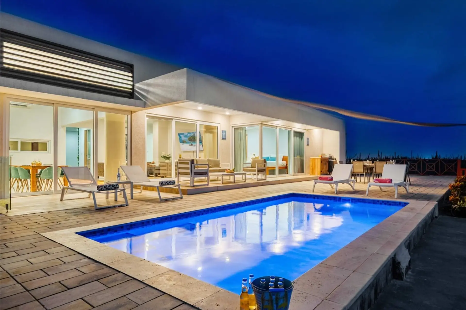 Gather beside the sparkling pool after sunset, where comfortable outdoor seating and a welcoming nighttime atmosphere set the stage for memorable vacation evenings.