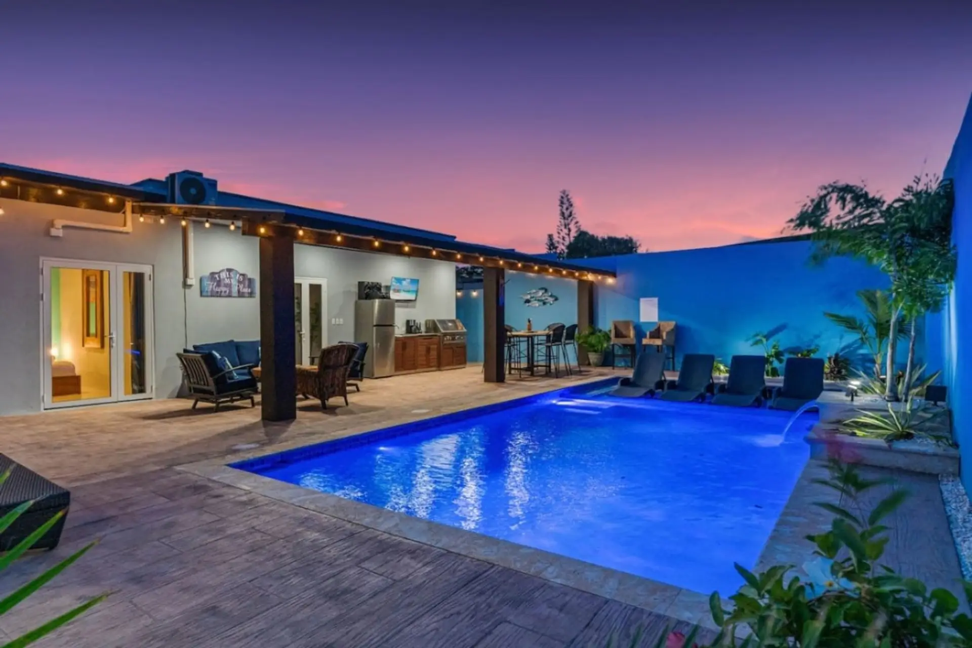 Unwind by the shimmering pool under twinkling evening lights, where a peaceful tropical setting creates the perfect spot for a refreshing evening escape.