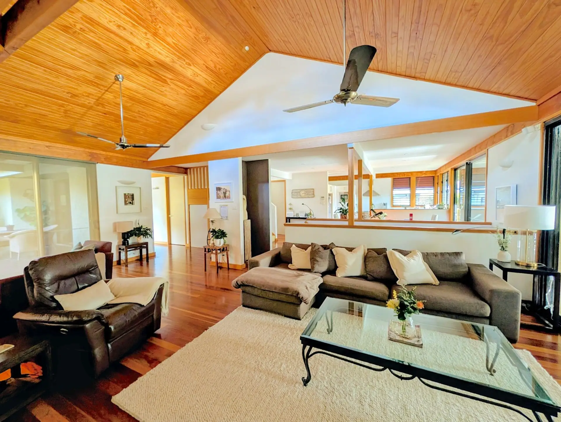 The full sweep of Maple Manor's open-plan living. Vaulted timber ceiling, dual ceiling fans, cozy fireplace with separate seating, lounge, flatscreen TV with soundbar, flows through to kitchen, front entertaining deck and rear courtyard.