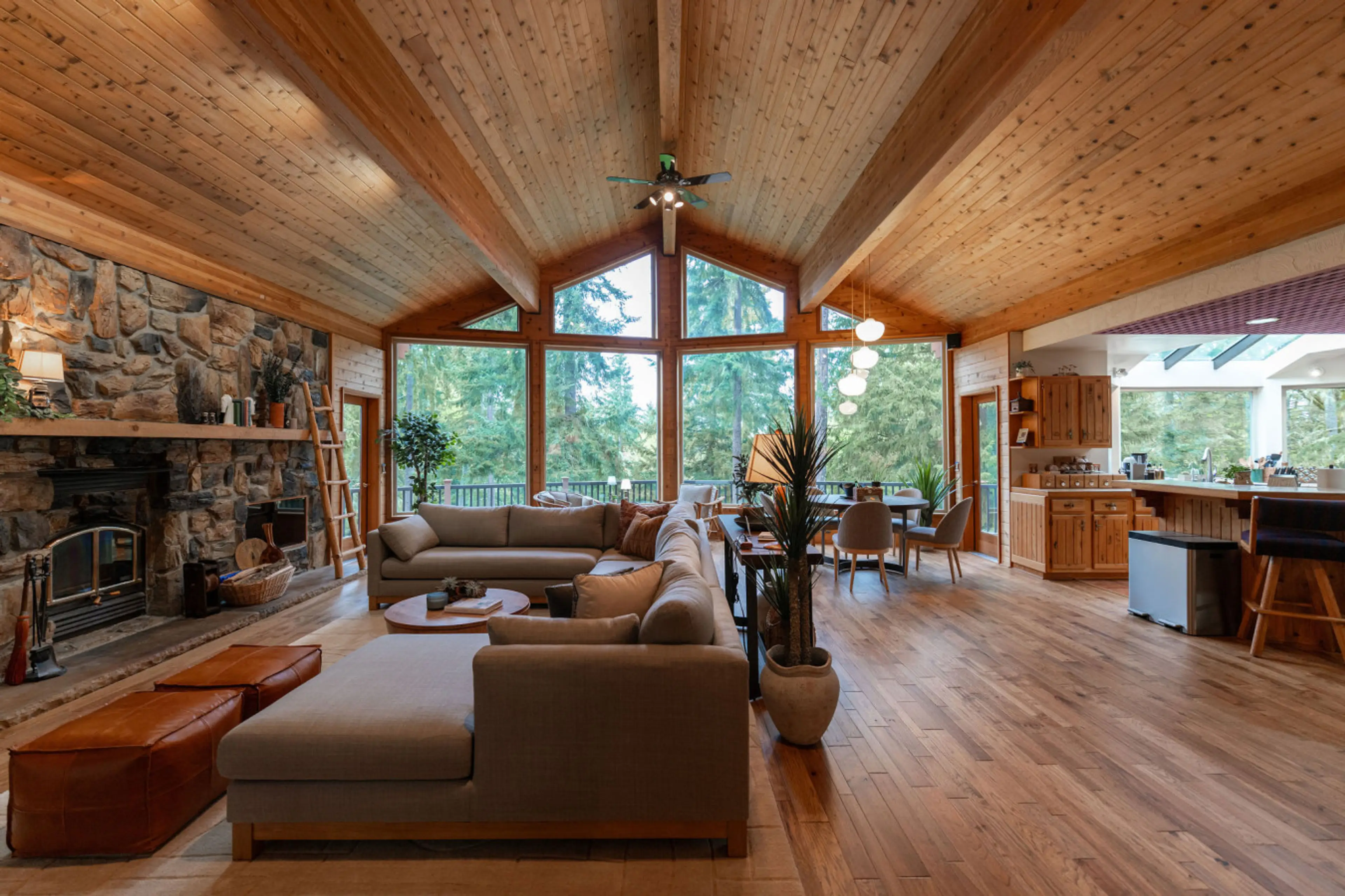 Open-concept great room with vaulted ceilings, panoramic forest views, and seamless living, dining, and kitchen flow