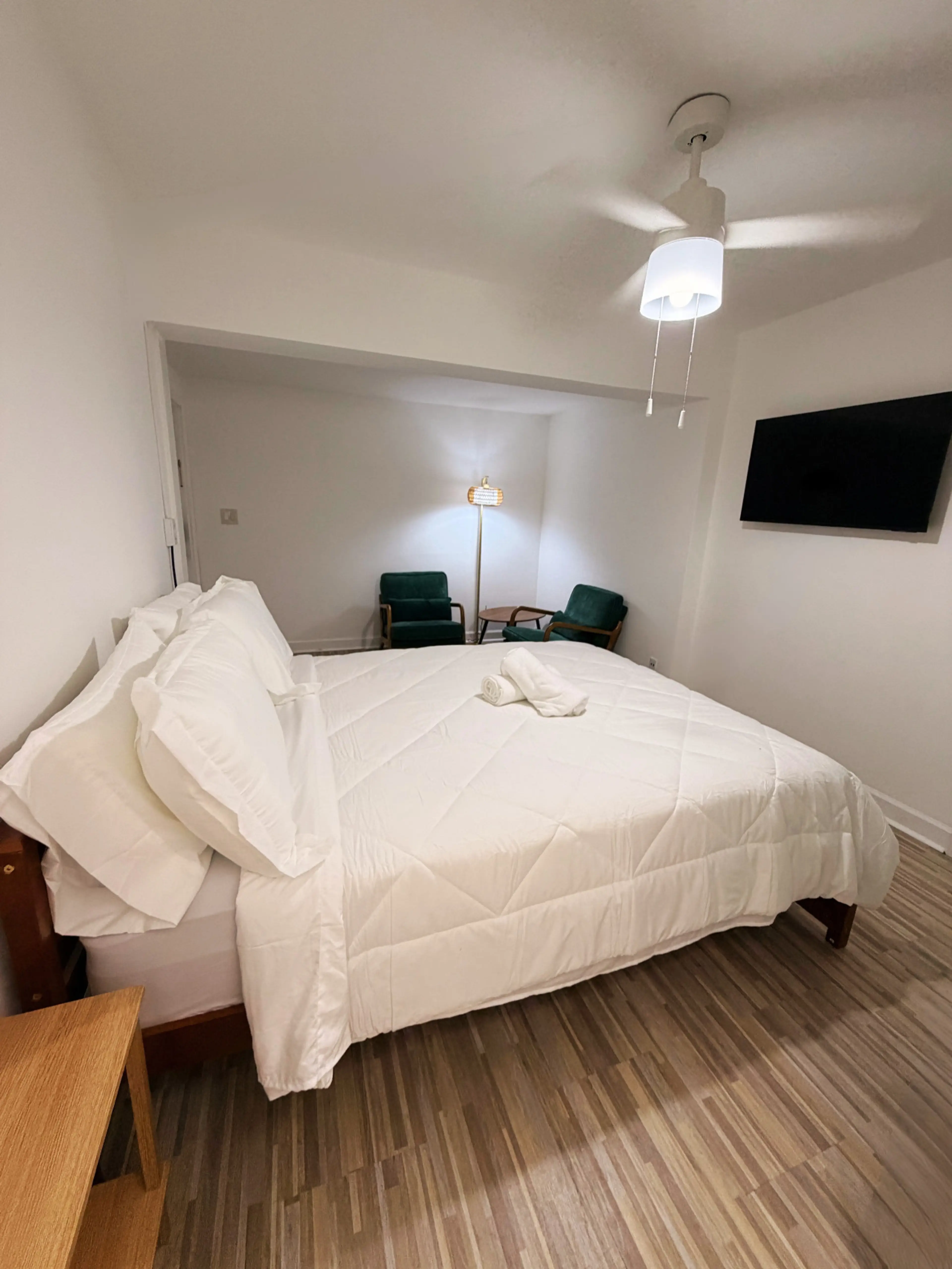 Bedroom with wall-mounted Smart TV, ceiling fan, and a relaxing sitting nook.