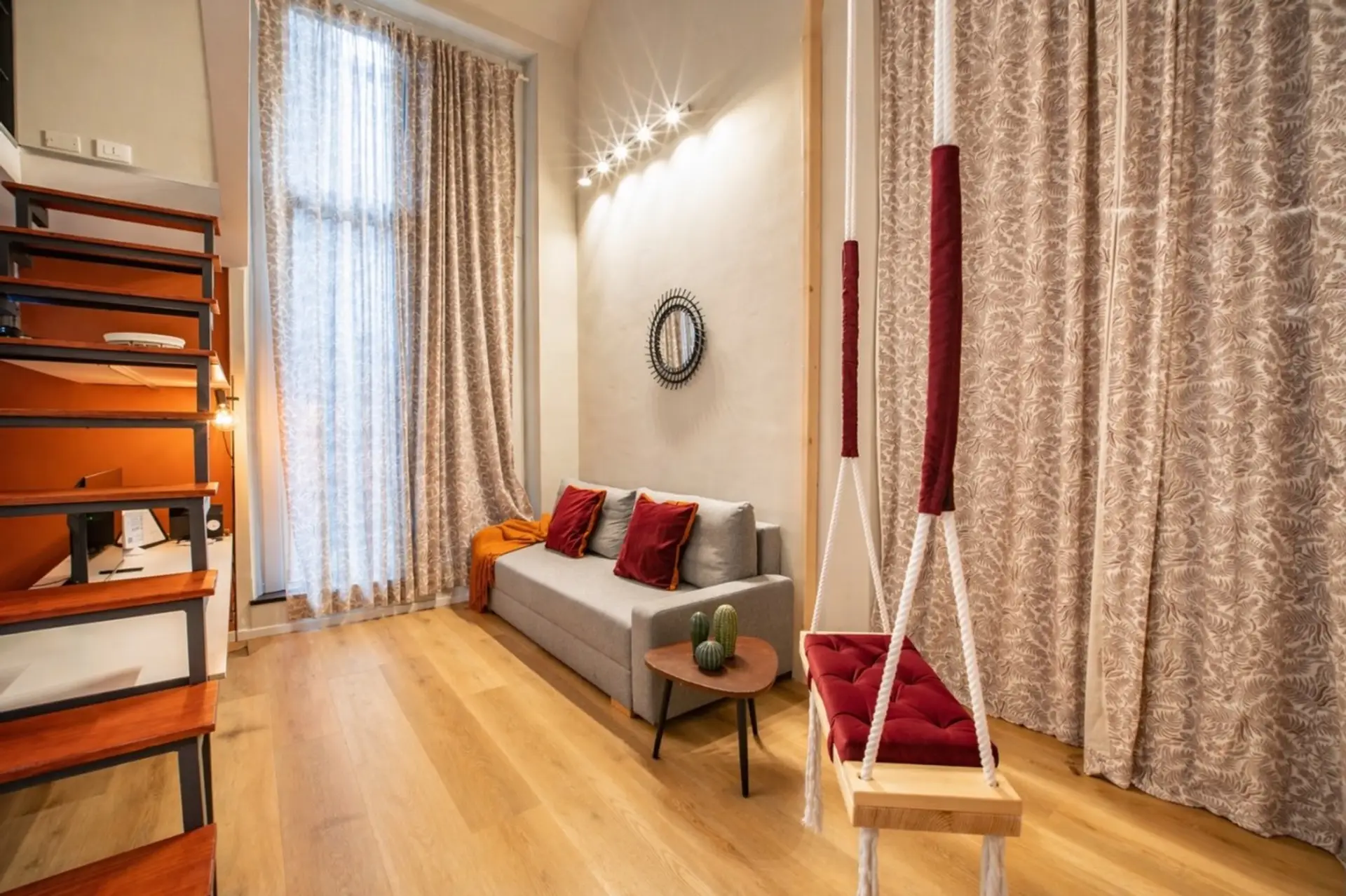 Zona living open space luminosa con scala di design a vista, divano accogliente e zona relax per due. Le grandi finestre portano luce naturale e collegano l’ambiente allo spazio esterno privato, nel centro storico di Genova.