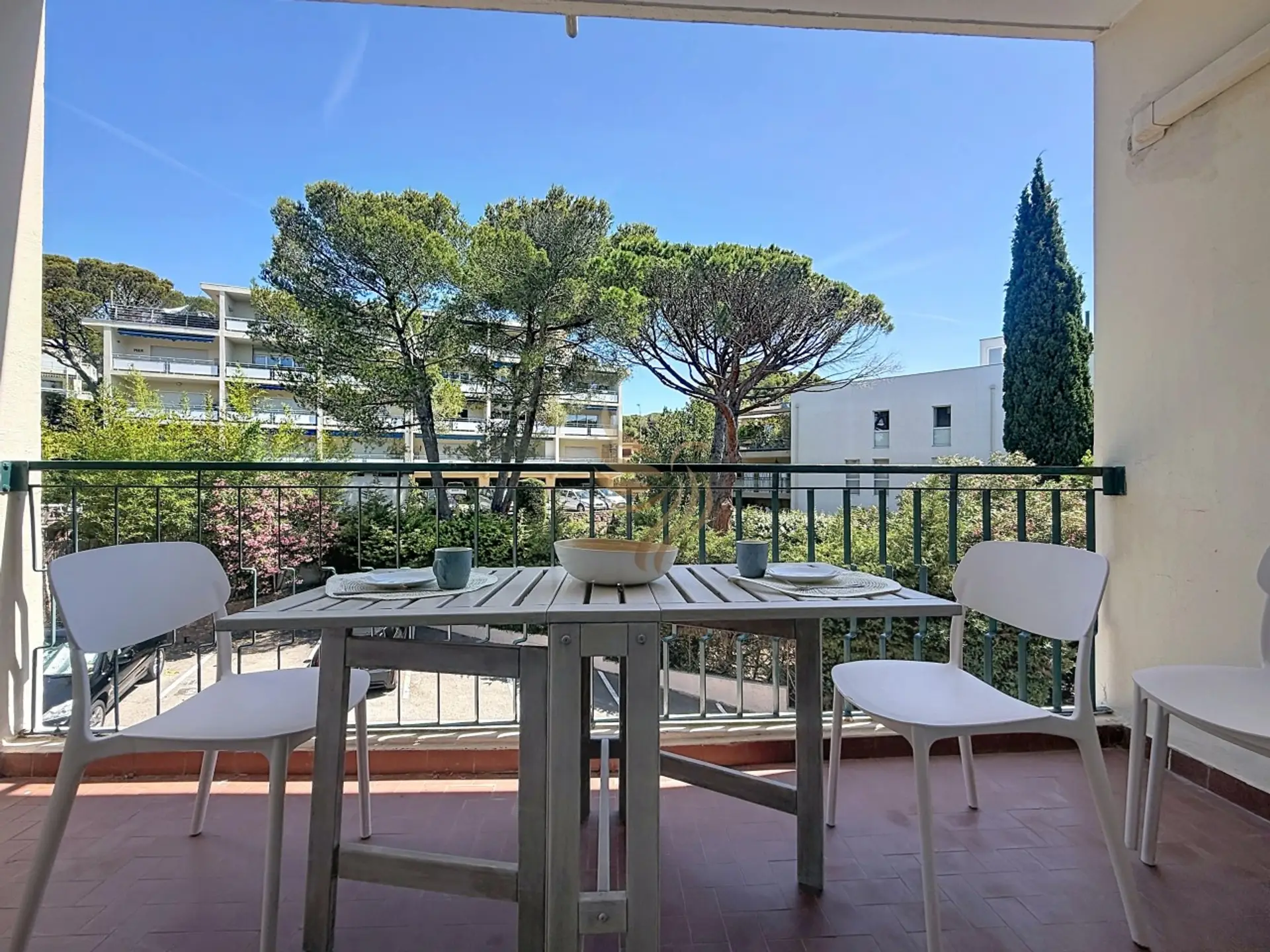 Imaginez votre petit-déjeuner ici : la table en bois grisé dressée pour deux, chaises blanches et vue sur les pins. Un matin ensoleillé, le calme du quartier, le point de départ idéal pour la journée.