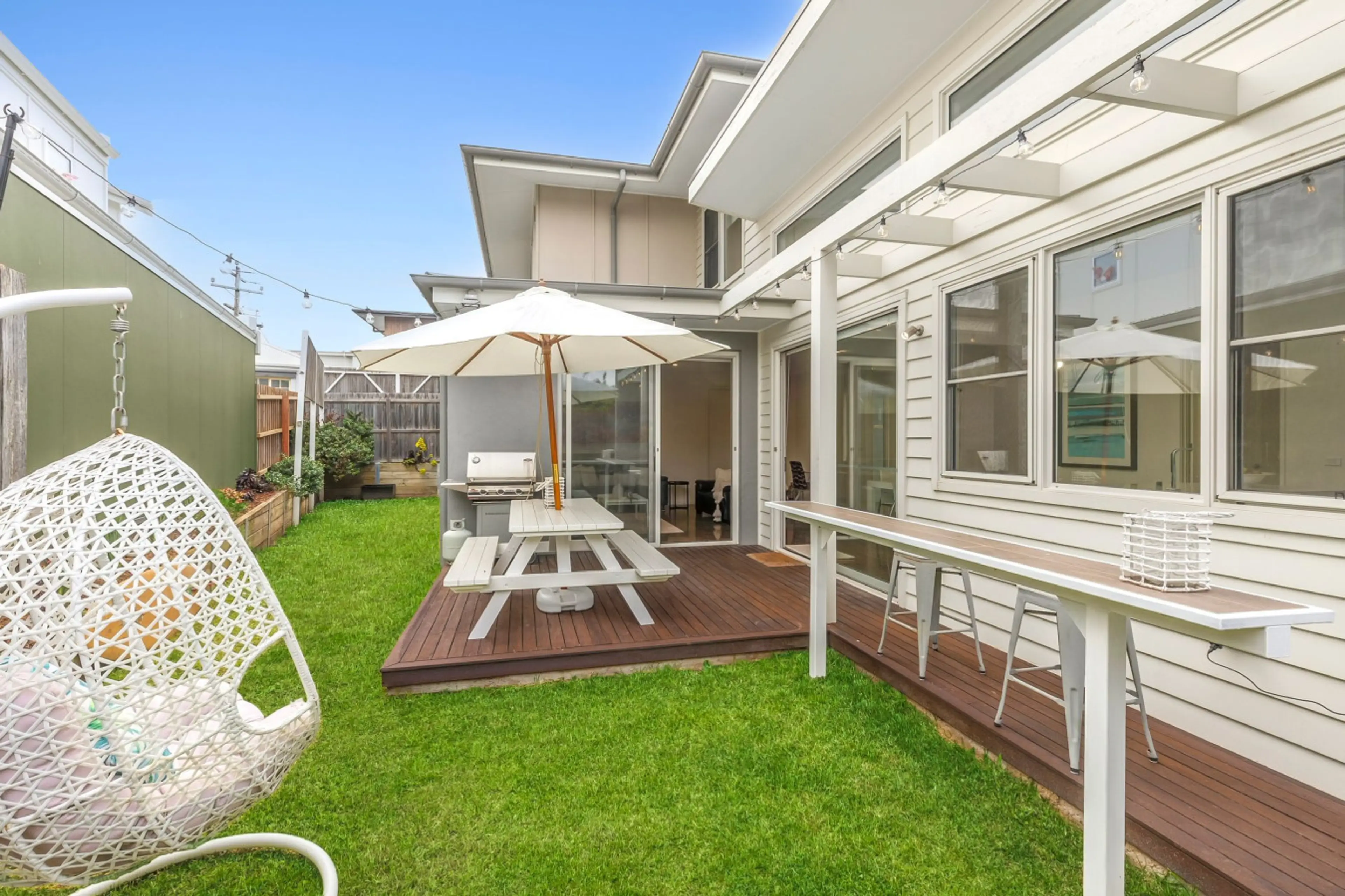 Green lawn, timber deck, BBQ, and hanging egg chair.