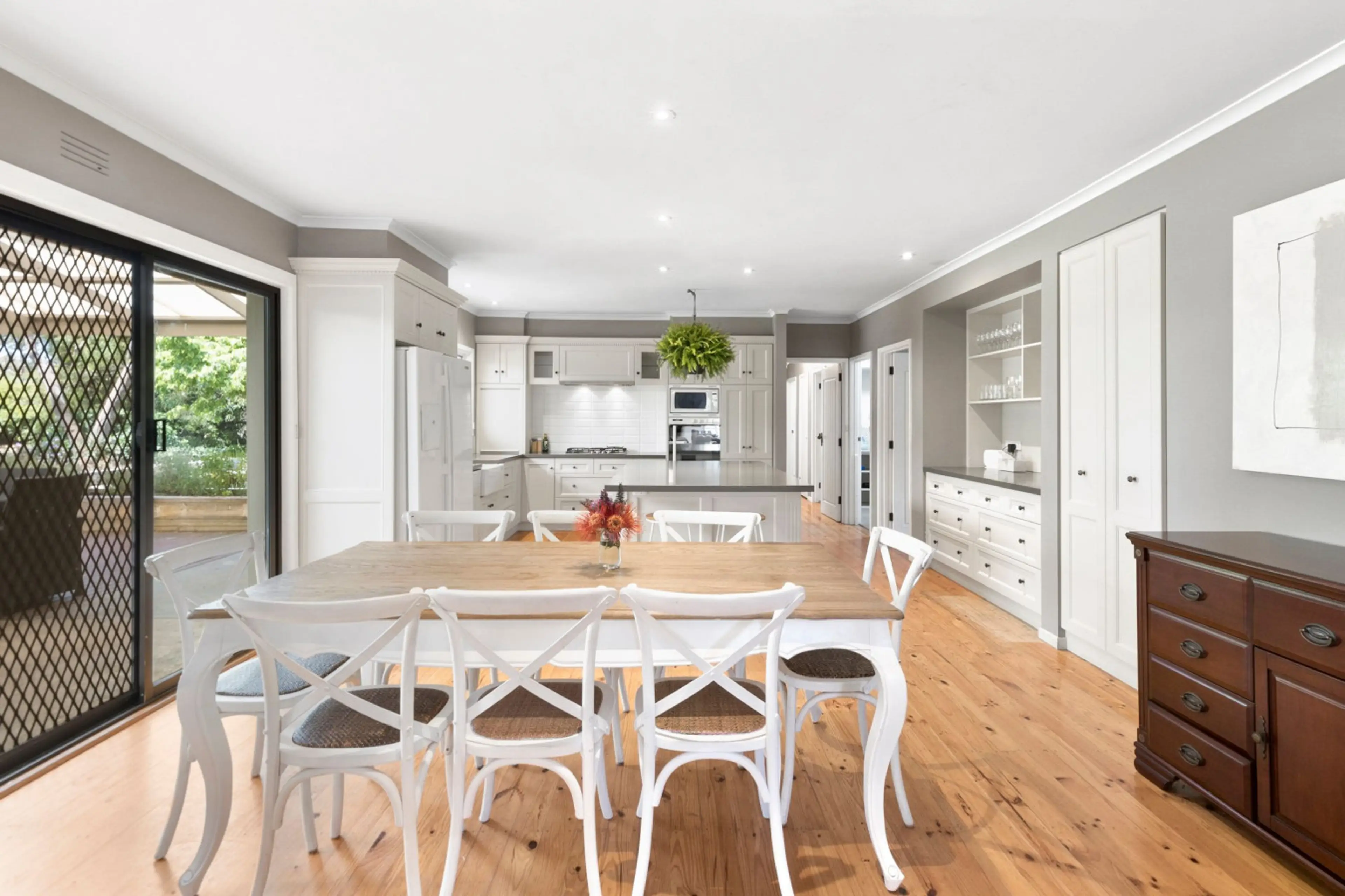 Spacious dining and kitchen with timber floors and white cabinetry.