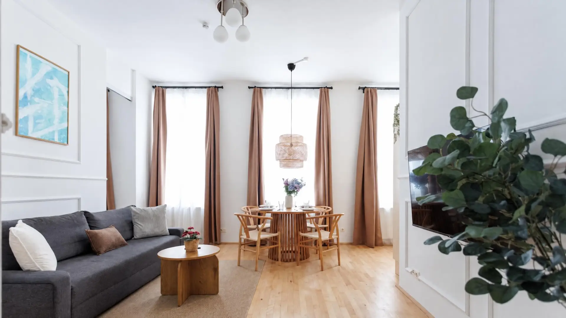 Willkommen im hellen Wohnzimmer der Ferienwohnung in Wien-Ottakring (1160): graues Sofa, runder Esstisch für vier, hohe Altbaufenster und Parkettboden