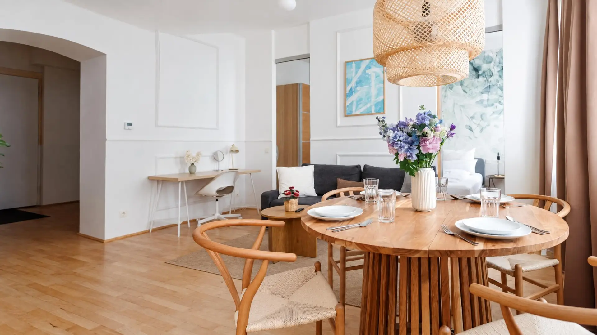 Gedeckter runder Esstisch für vier mit Blumenstrauß unter der geflochtenen Pendelleuchte, dahinter die Küchenzeile der Altbauwohnung in Wien-Ottakring