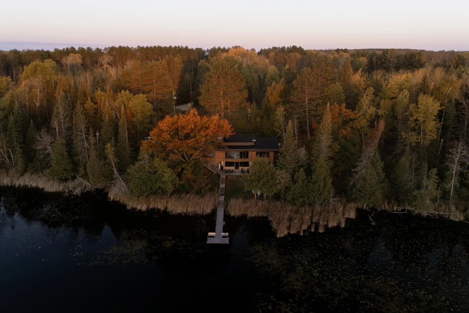 The house at dusk, lit from inside with the dock waiting below.
