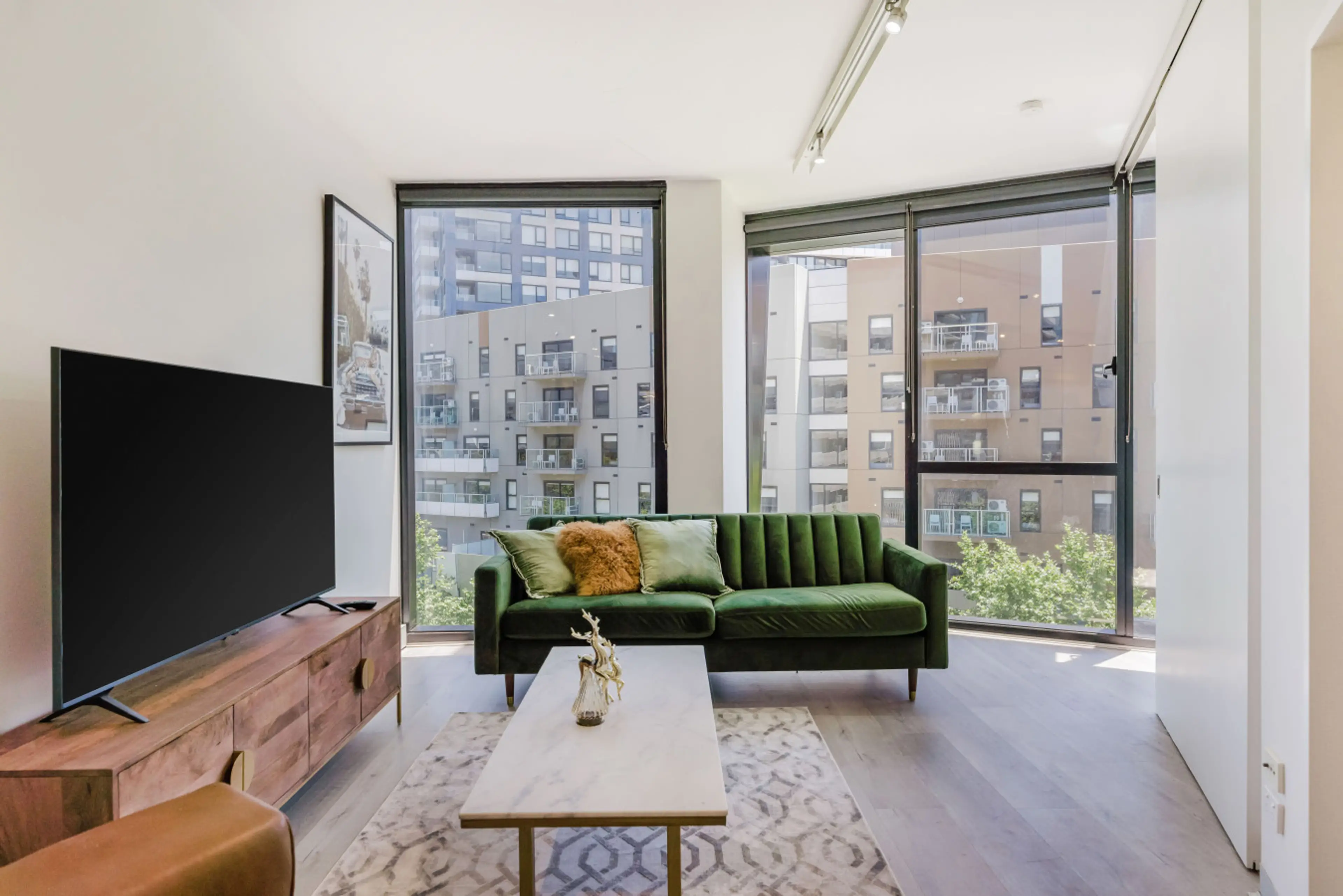 Cozy living room with a green sofa, large TV, and a city view.
