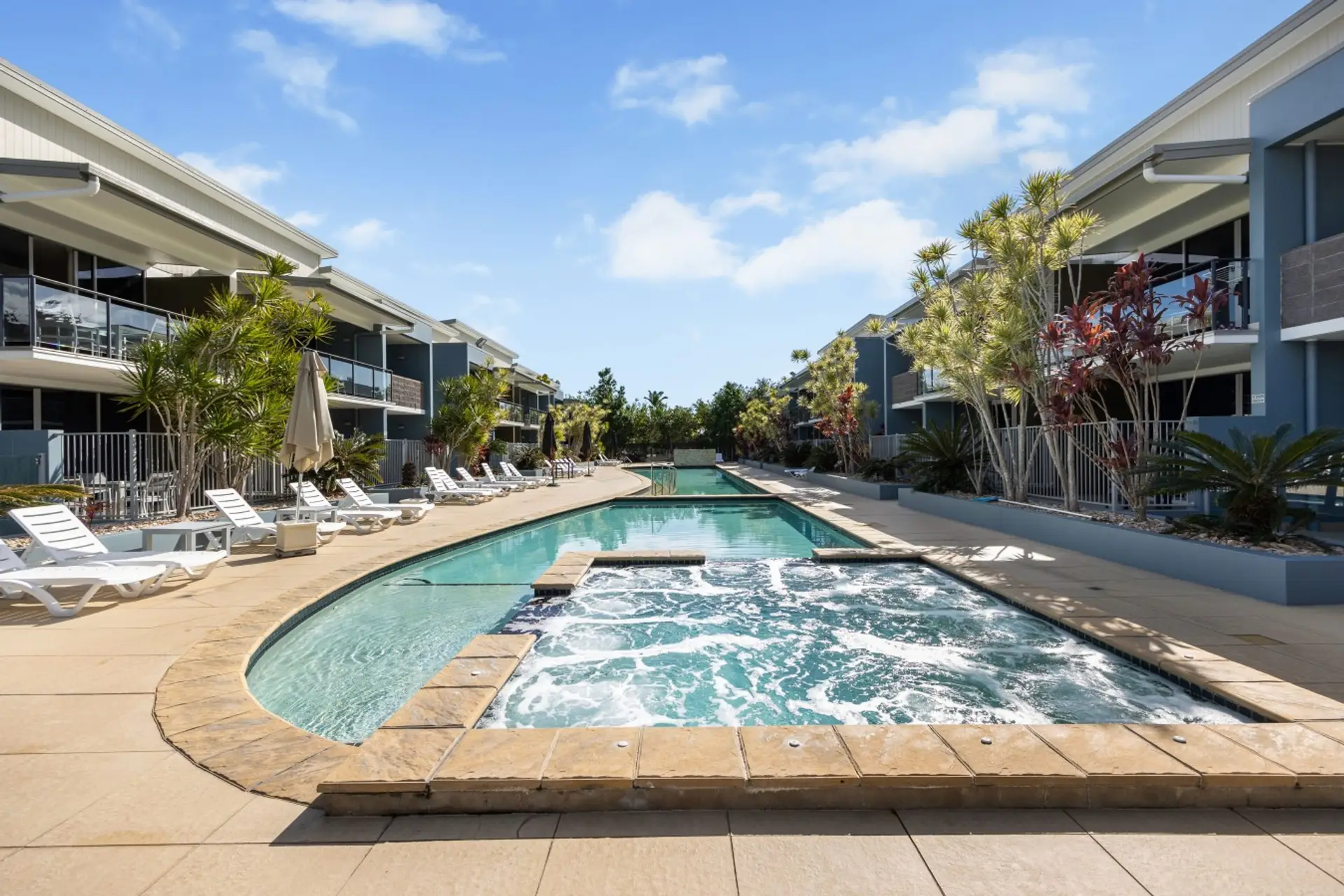 Sparkling resort-style pool and spa surrounded by palm trees and sun loungers — your daily holiday ritual starts here.