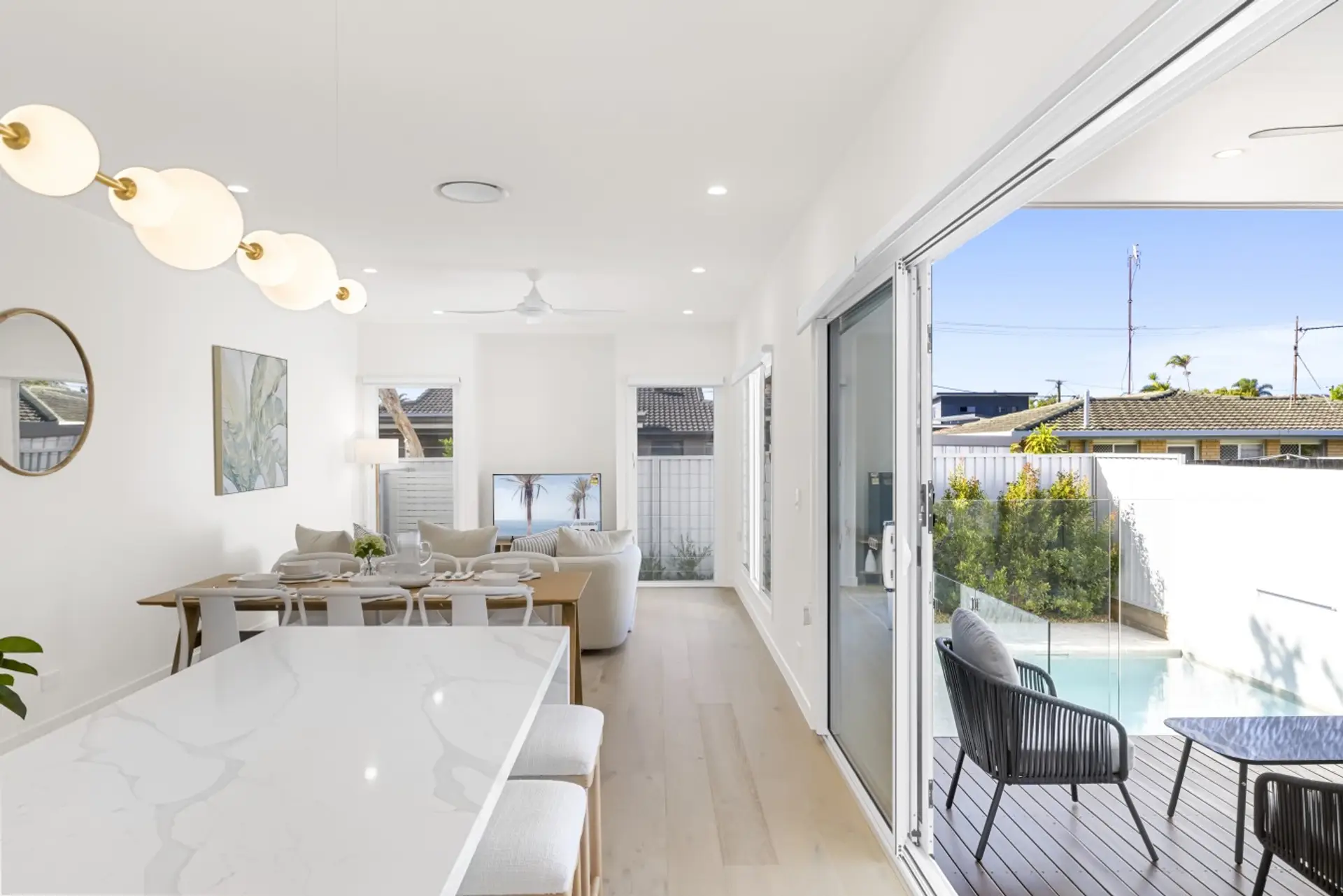 A vast, light-filled open-plan dining and living space with designer pendant lighting, long marble table, and sliding doors opening straight to the pool and alfresco.