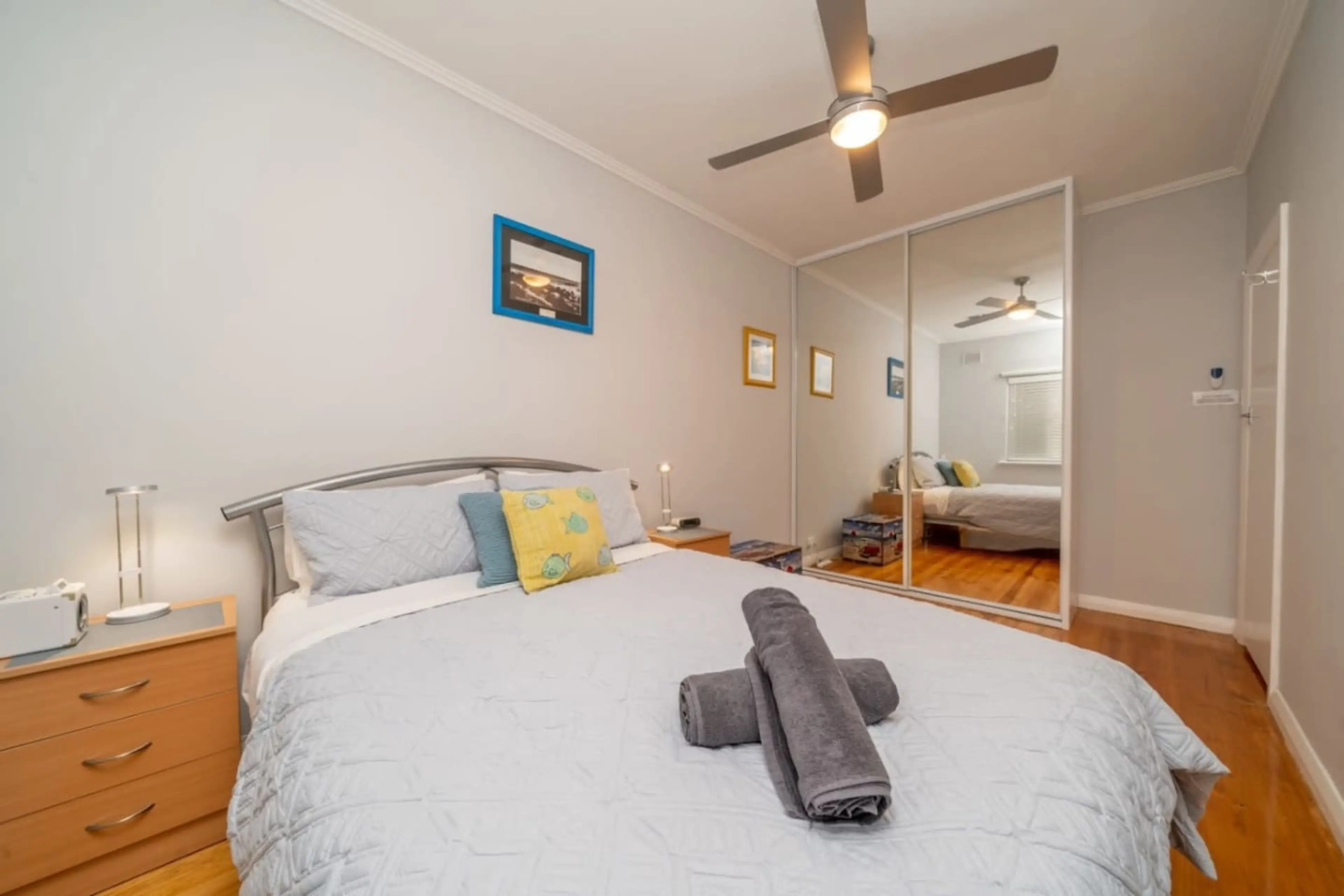 A comfy queen bed framed by mirrored wardrobes and warm timber floors.