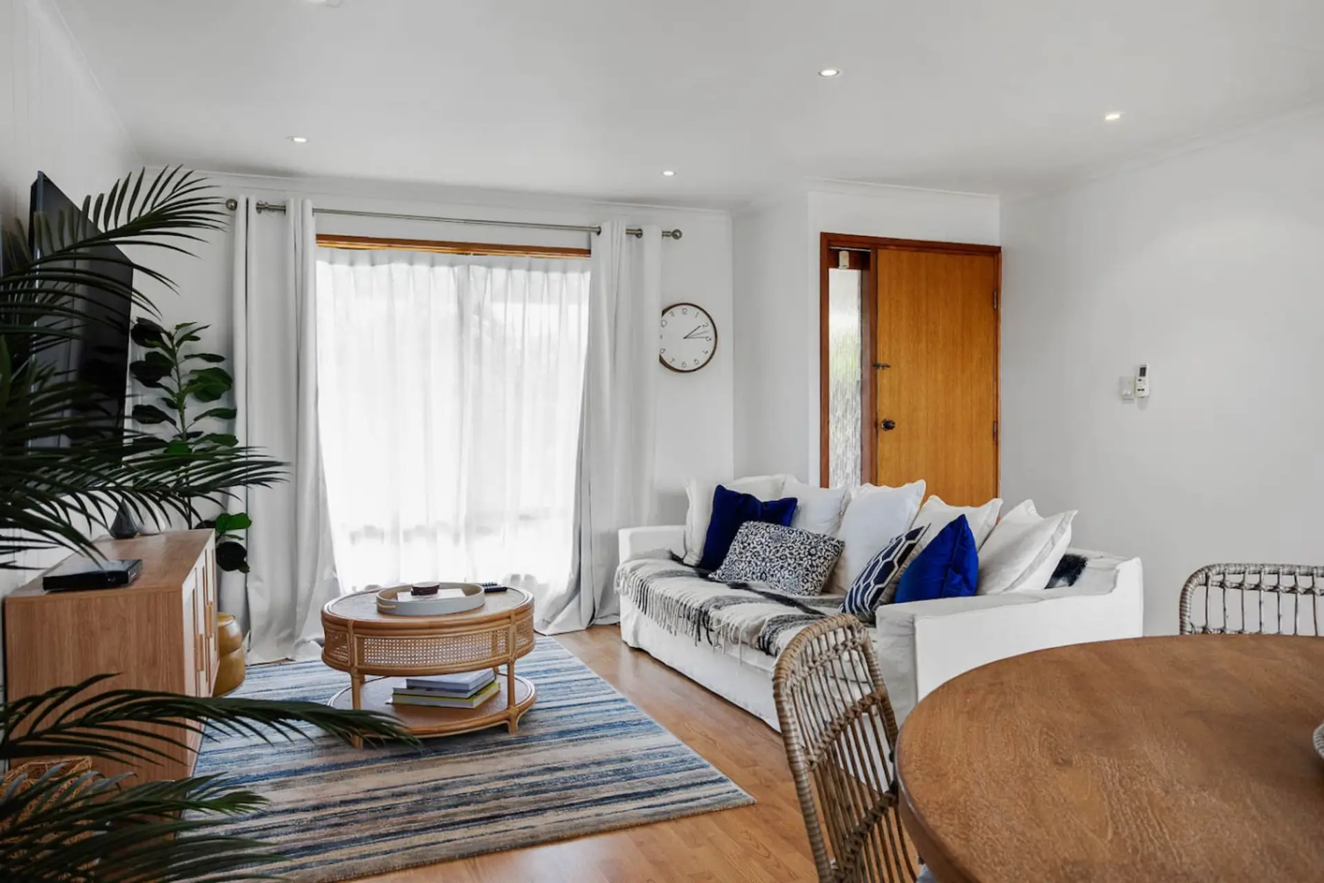 A bright and welcoming lounge styled in Hamptons-inspired tones, featuring plush sofas, layered textures, and a large wall-mounted TV for relaxed evenings in.