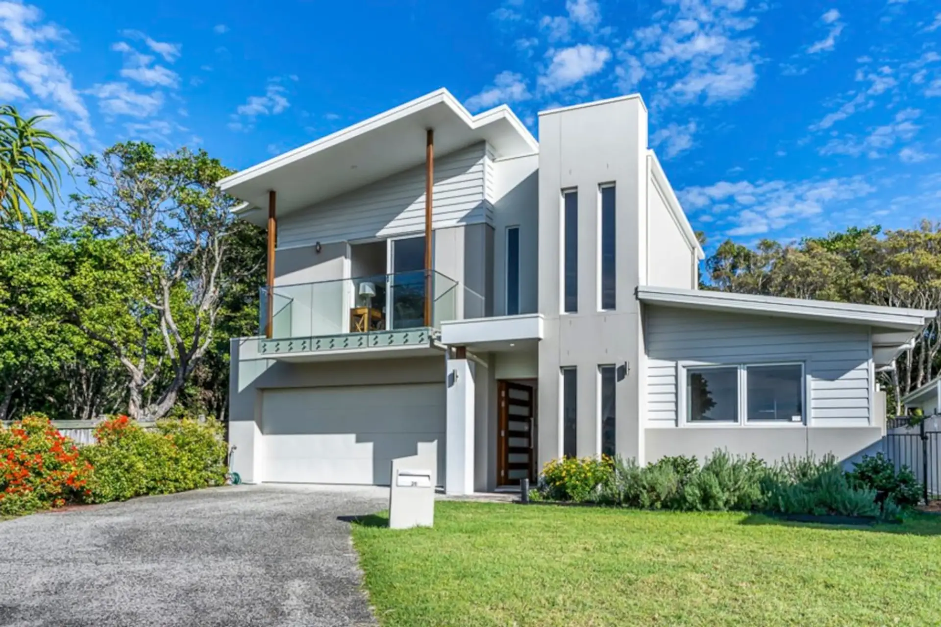 Sunlit two-storey modern exterior with double garage, timber-accent columns, and lush garden — a striking first impression