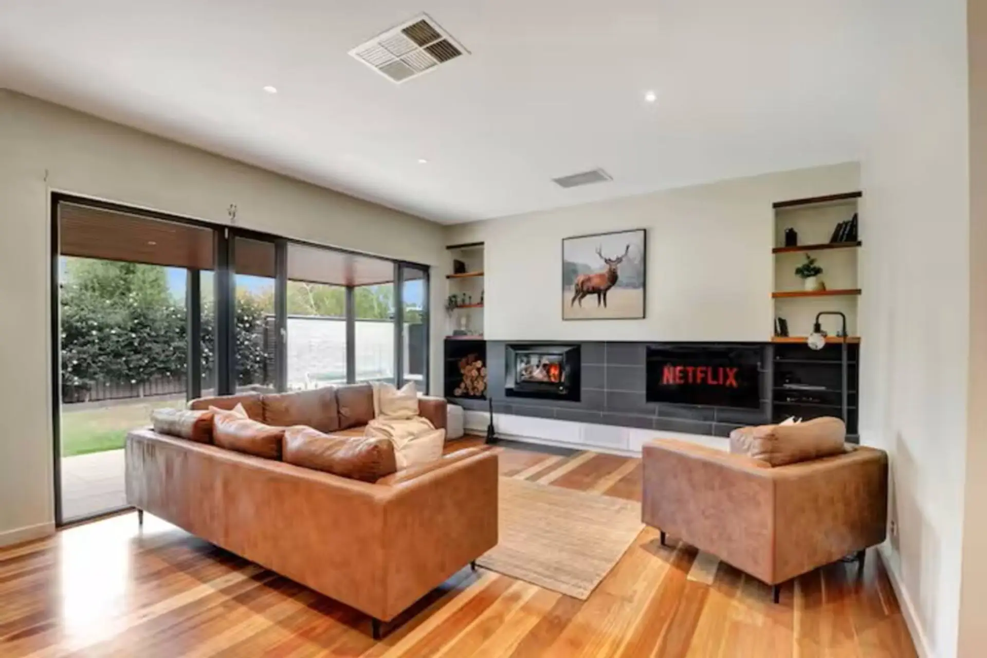 Modern living room with wood fireplace, leather seating and garden outlook at Banksia House High Country Retreat holiday home in Mansfield, Victoria’s High Country