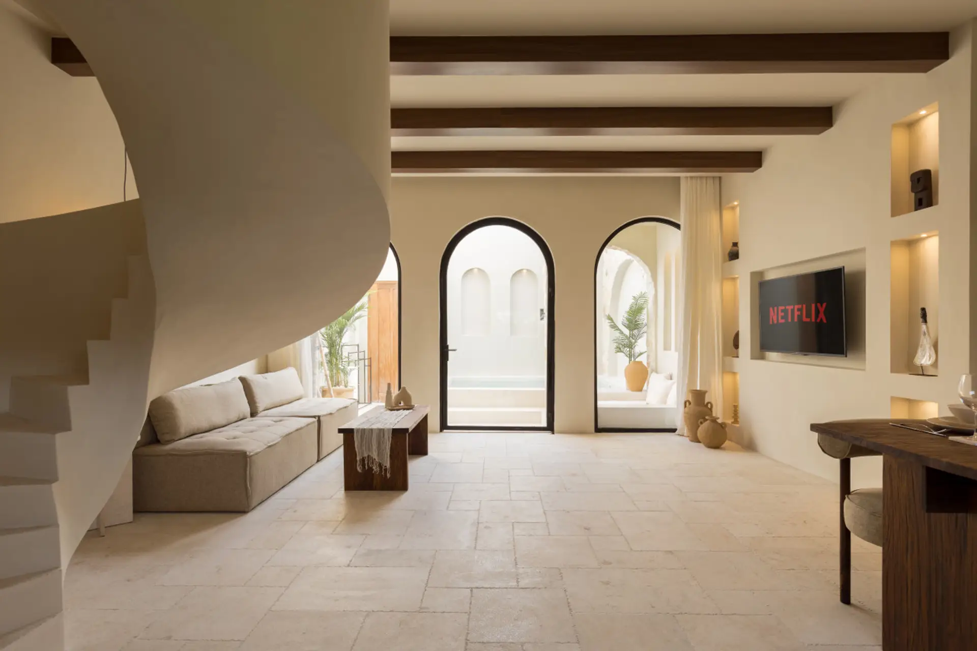 Earthy Mediterranean living room with sculptural stairs, natural textures, and soft light through arched doors.