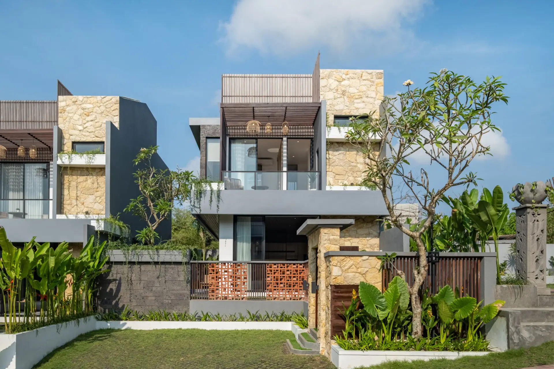Modern tropical villas with stone and wood accents are surrounded by lush greenery, creating a serene and luxurious atmosphere.