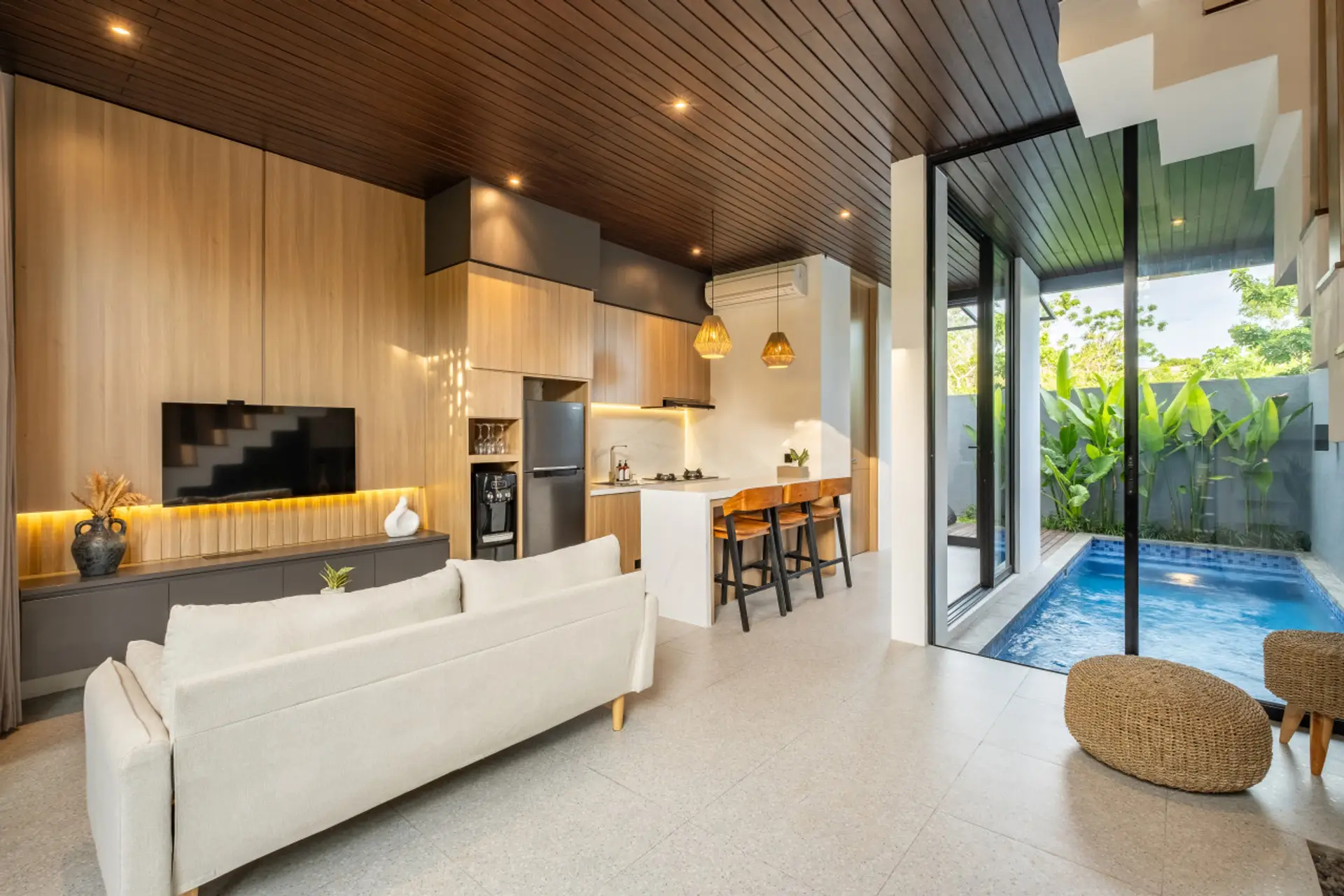 Modern open-plan living space with wood accents, pool view, and sleek kitchen.