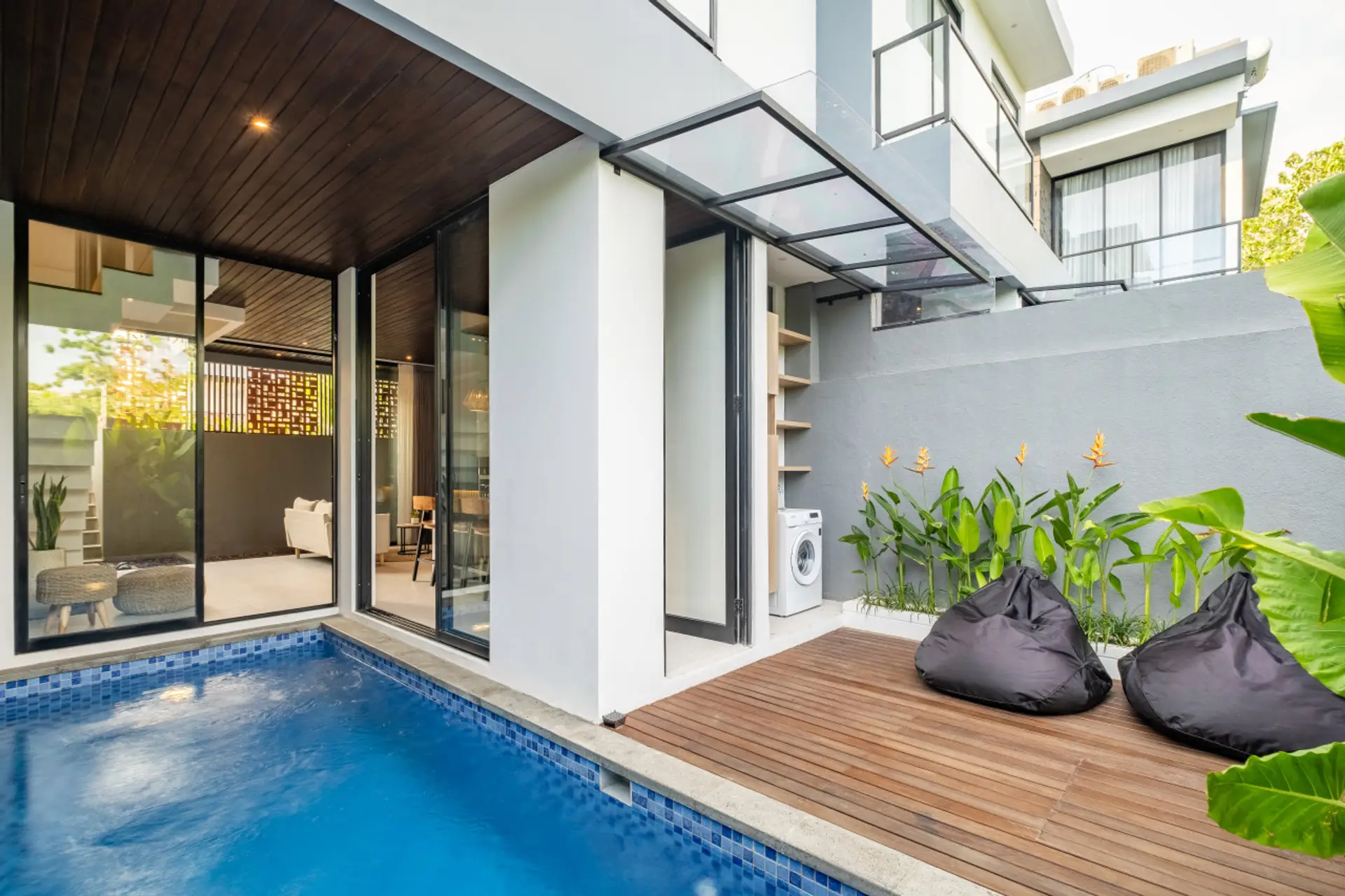 A modern outdoor space with a small pool, wooden deck, tropical plants, and a cozy bean bag—blending relaxation and style.