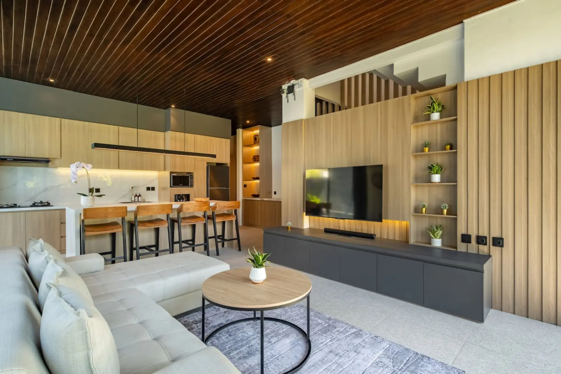 A bright, modern living area with a cozy sofa, stylish kitchen with bar seating, and large glass doors overlooking a private pool.