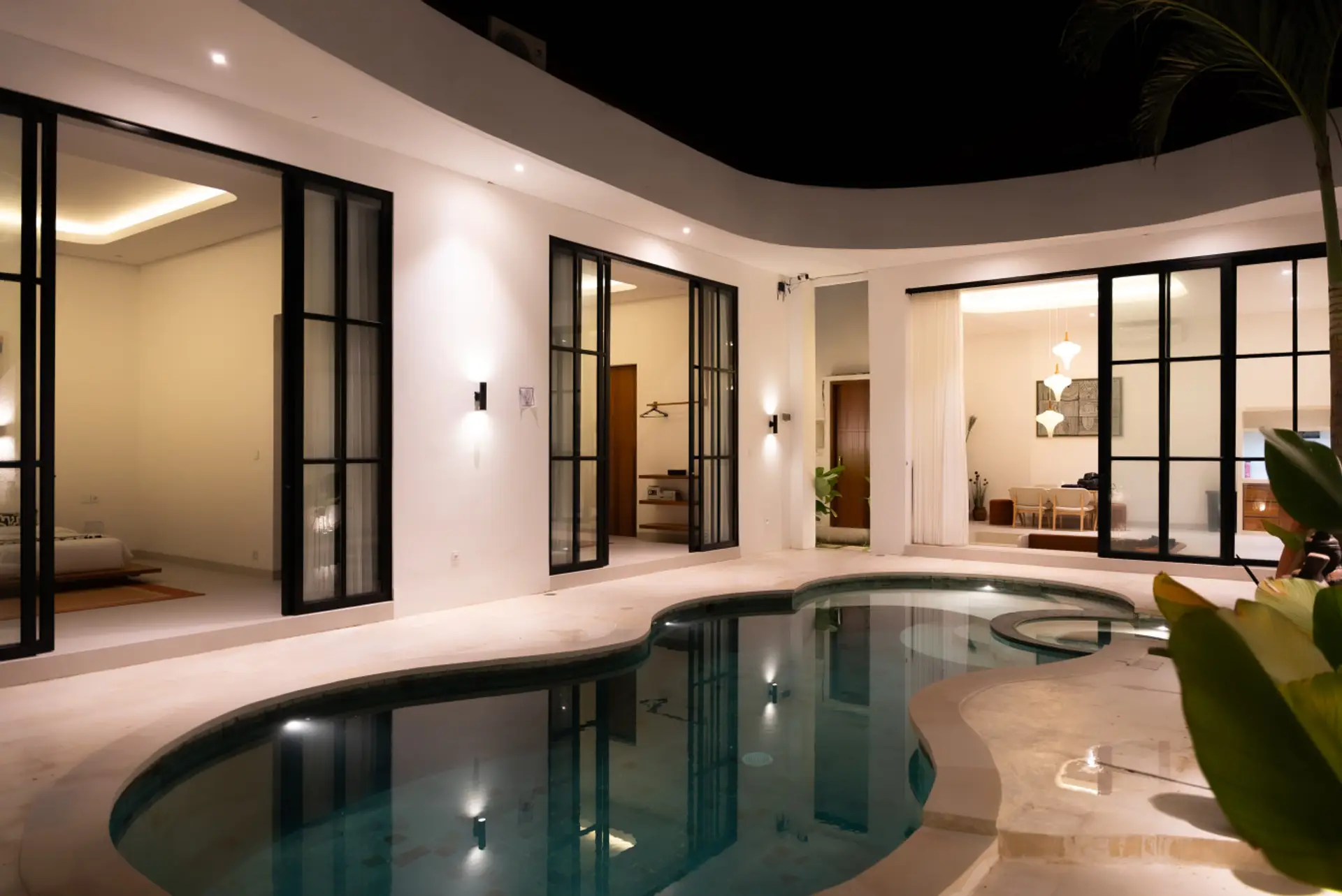 Modern tropical retreat featuring a private freeform pool with jacuzzi, surrounded by lush greenery and seamless indoor-outdoor living through large sliding glass doors.