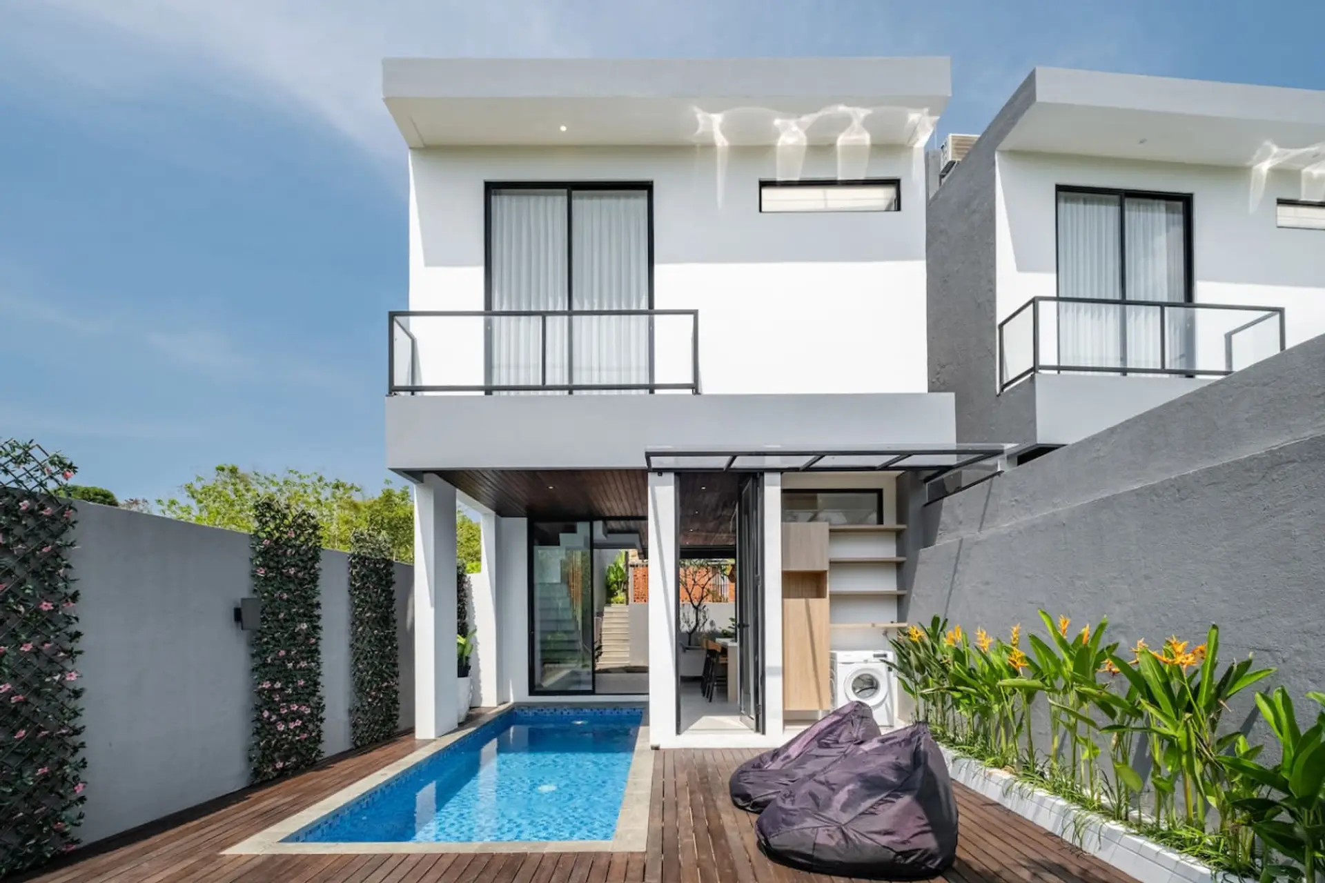 A modern outdoor space with a small pool, wooden deck, tropical plants, and a cozy bean bag—blending relaxation and style.