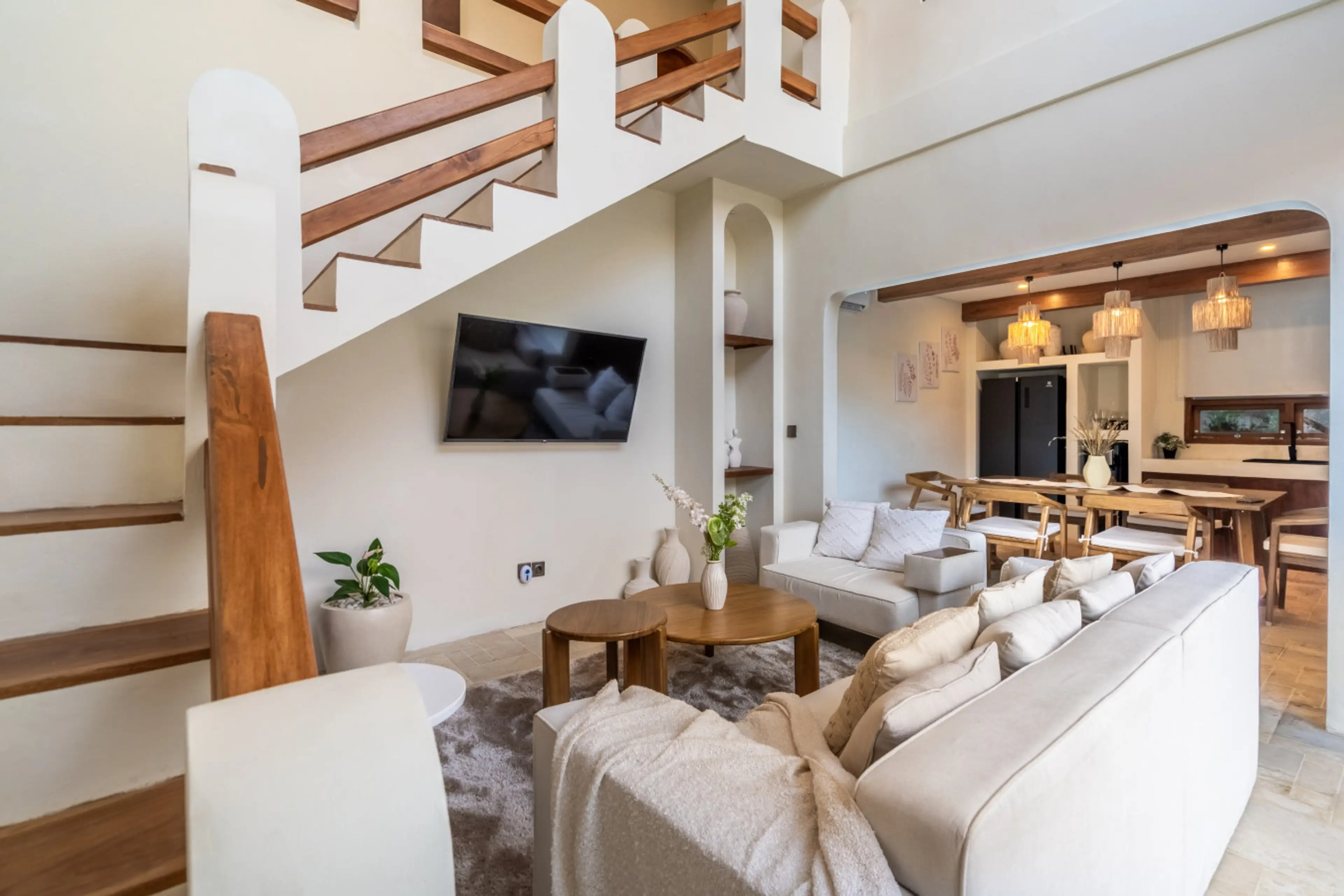 A modern living area features a wooden staircase, a comfortable sofa, a wall-mounted TV, and a dining space.