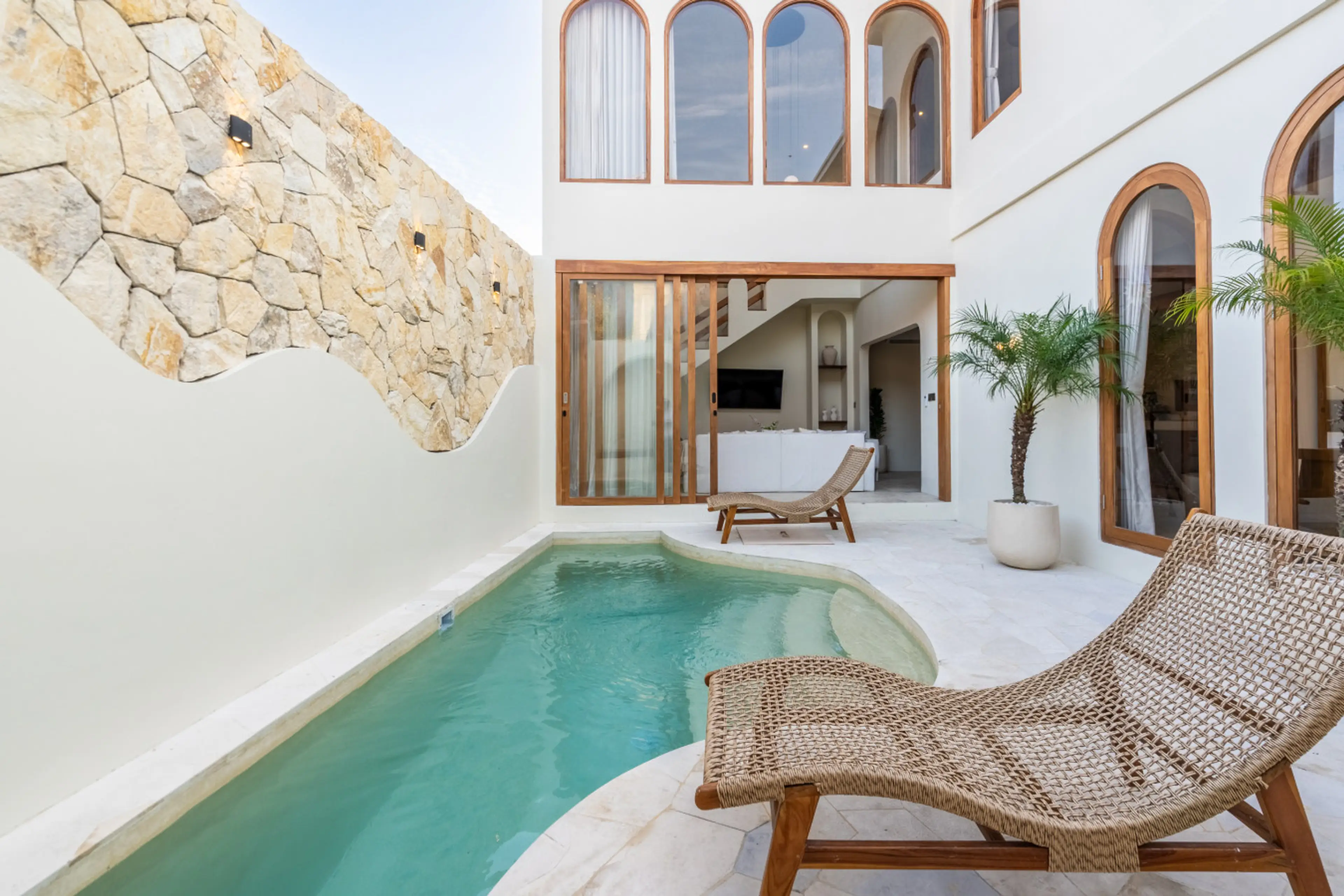 A villa courtyard with a swimming pool, a sun lounger, and potted palm trees.