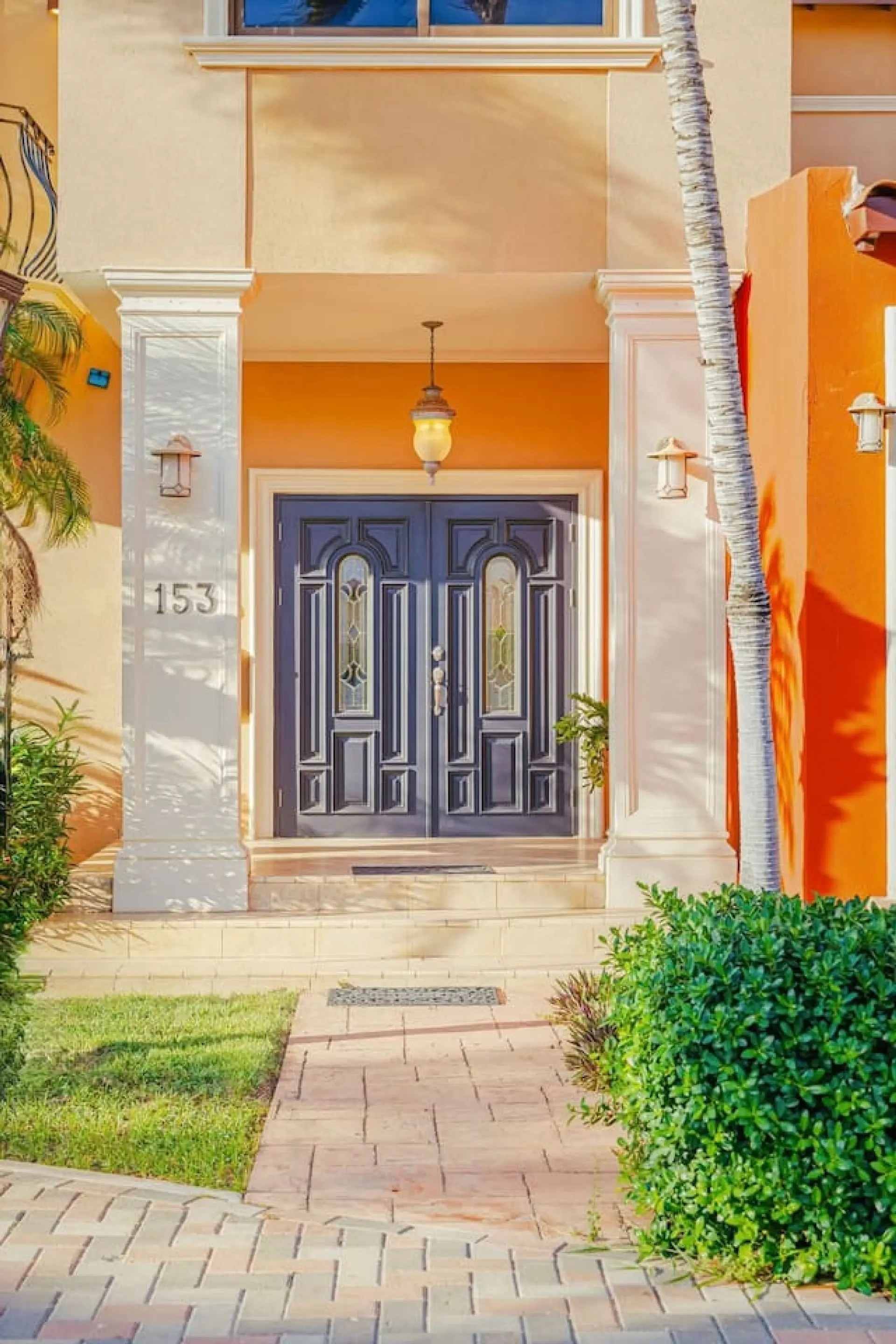 Bold orange walls and a deep blue double door create a stunning contrast, glowing warmly under a vintage hanging lantern.