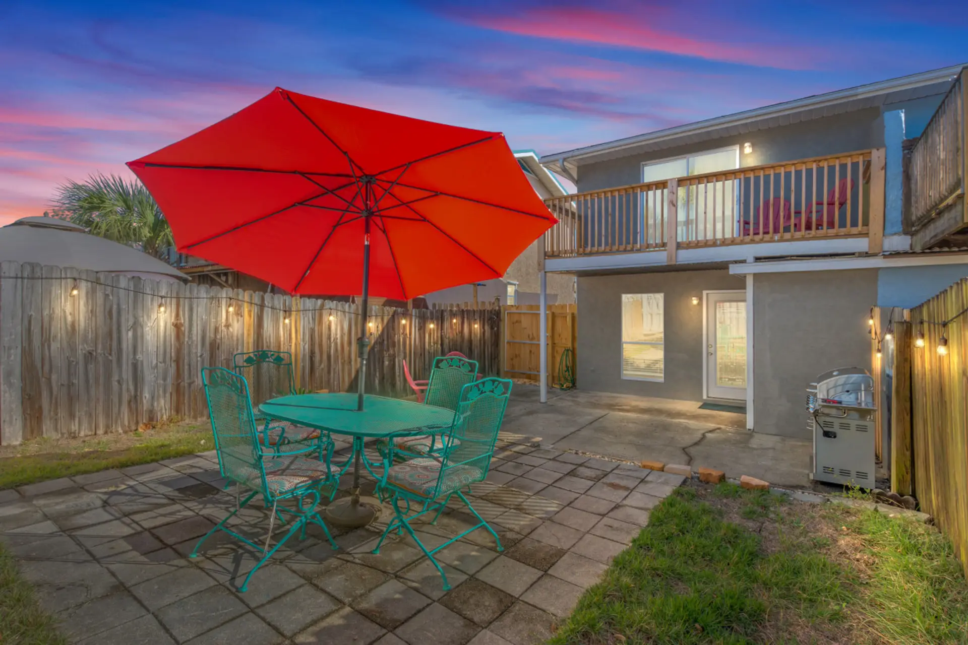 The backyard comes alive at sunset, with twinkling Edison lights illuminating an umbrella table and seating area—ideal for peaceful evenings with family or friends.