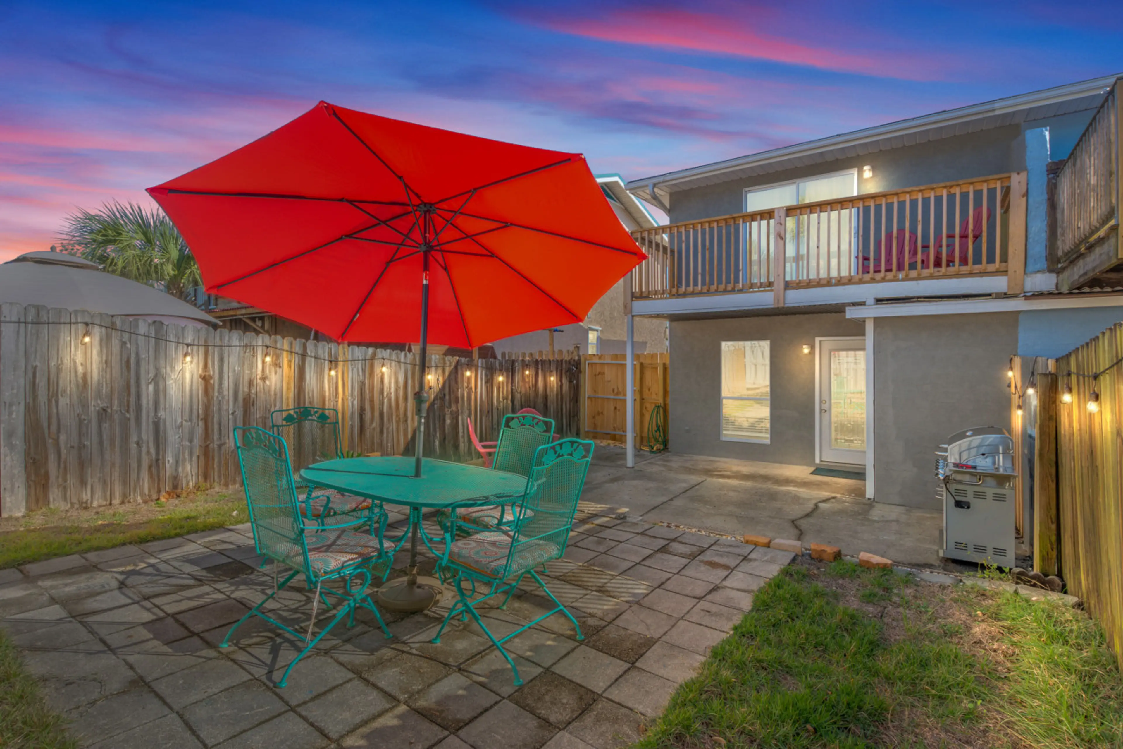 The backyard comes alive at sunset, with twinkling Edison lights illuminating an umbrella table and seating area—ideal for peaceful evenings with family or friends.