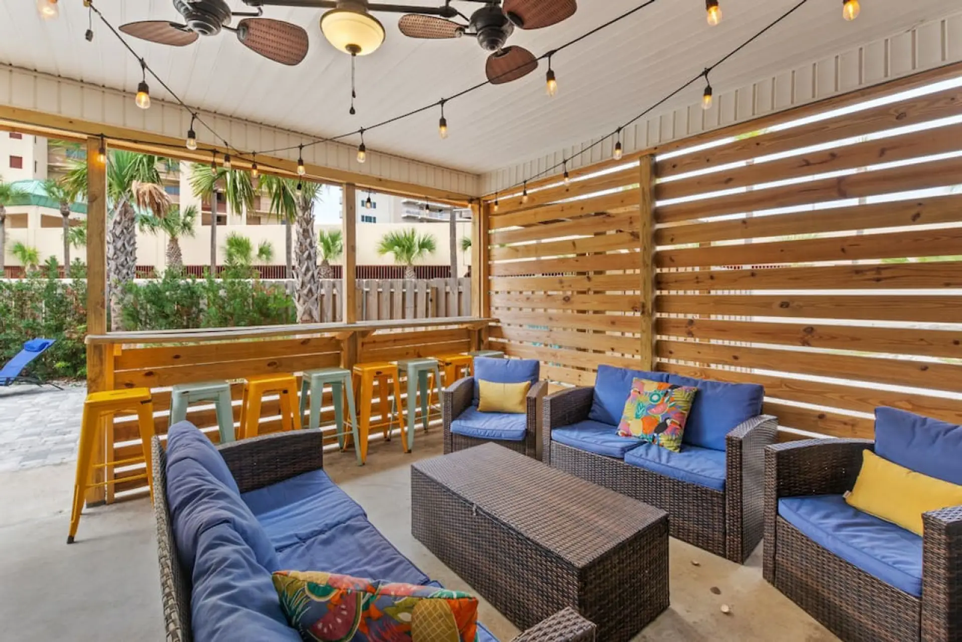 Covered seating on the pool deck, with fans, Edison lights, bar & bar stools, picnic table, outdoor shower, & swing