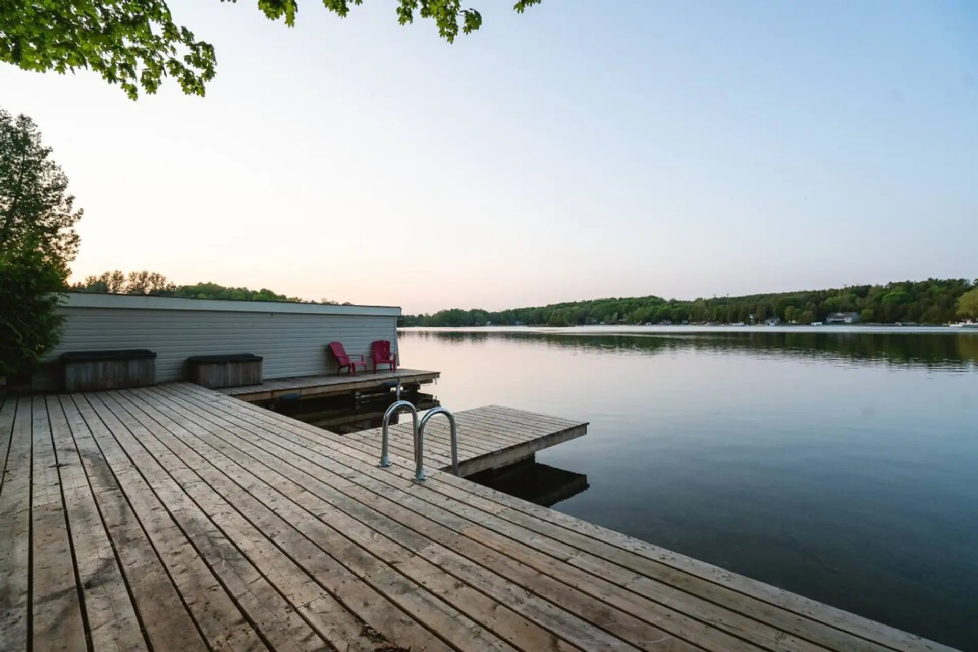 Step onto the wide wooden dock and feel the stillness of the water surround you. The air is fresh, the lake is calm, and the horizon stretches out in quiet beauty. Those red chairs are waiting for unhurried conversations, morning coffees, or simply a mome