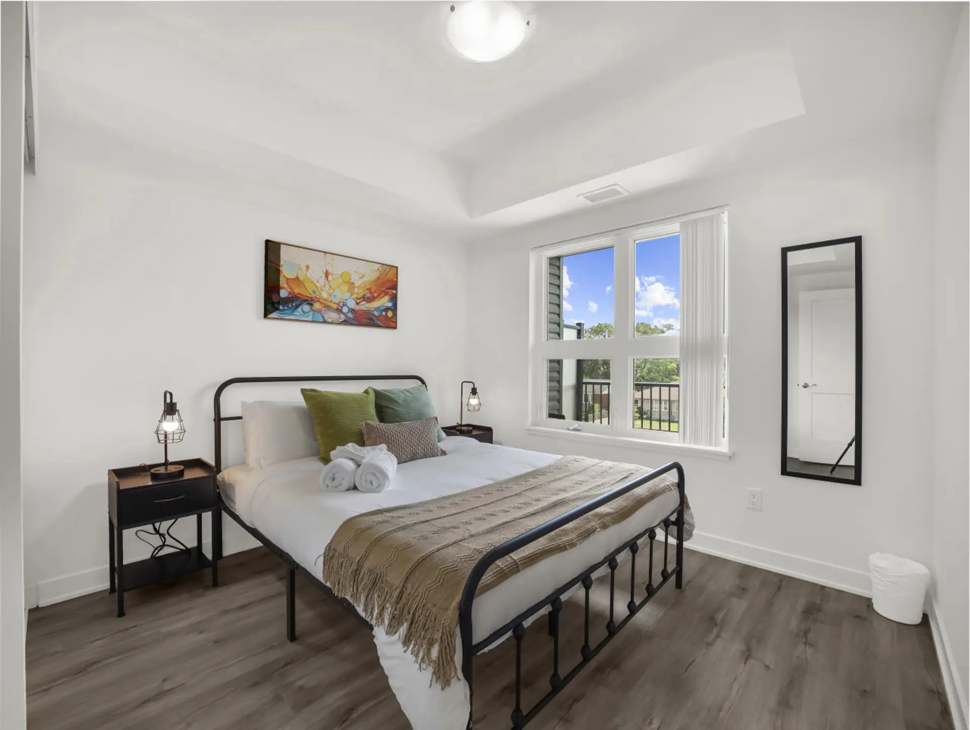 A peaceful retreat awaits. This bright, modern bedroom features a comfortable queen bed, stylish metal frame, cozy throws, and colorful art for a relaxing stay.