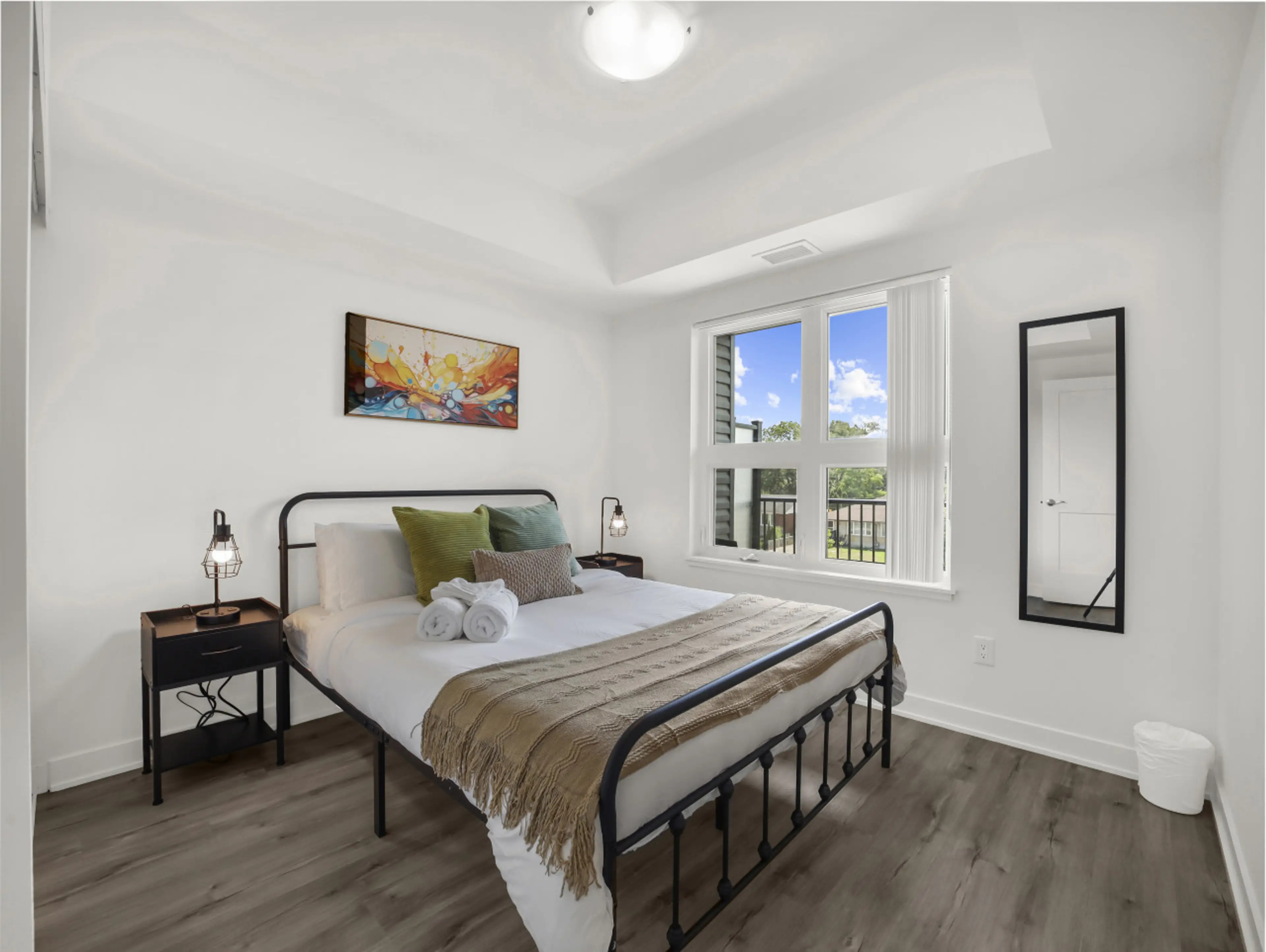 A peaceful retreat awaits. This bright, modern bedroom features a comfortable queen bed, stylish metal frame, cozy throws, and colorful art for a relaxing stay.