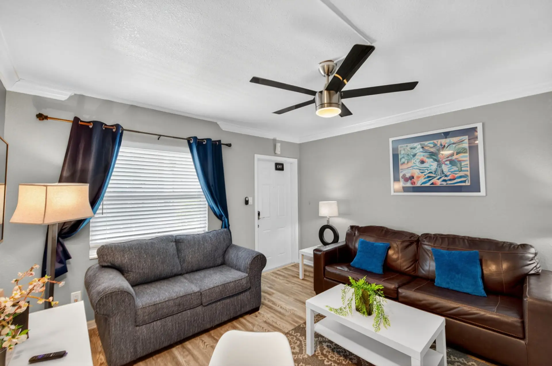 Bright living area w/ comfy seating, ceiling fan & calming blue accents for laid-back lounging.