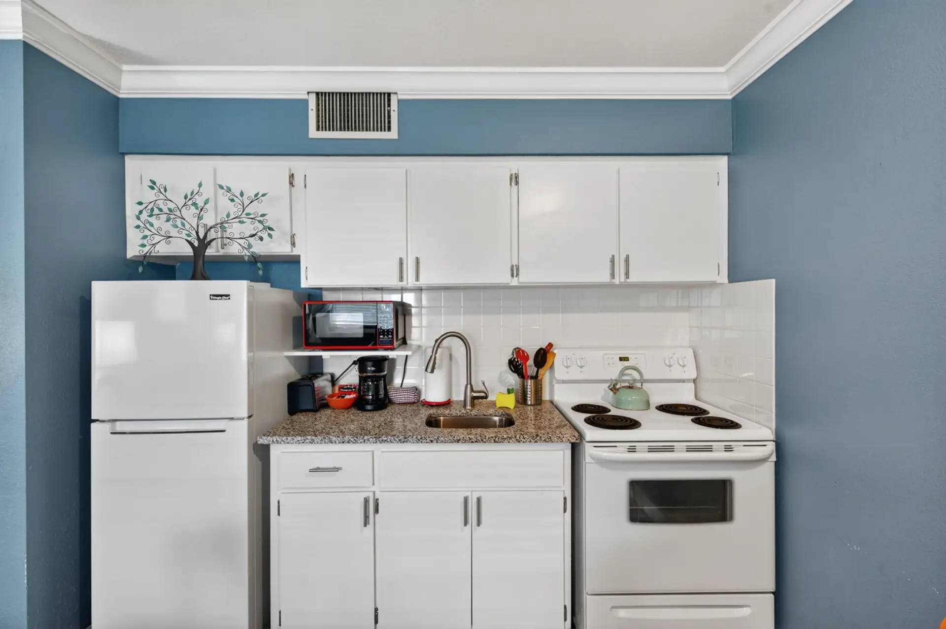 Clean, compact kitchen w/ white cabinets & everything set up for simple meals at home.