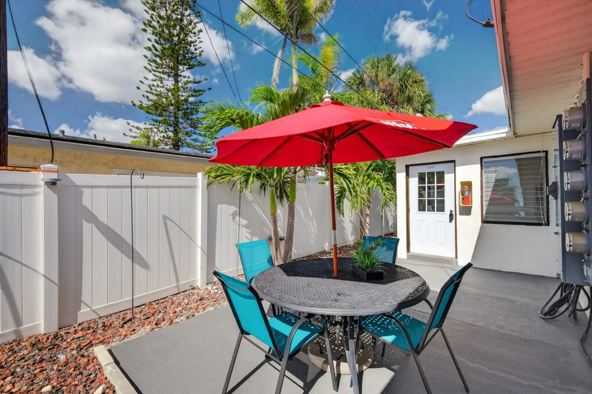 Bright patio w/ red umbrella & bistro seating, ideal for relaxed outdoor meals.