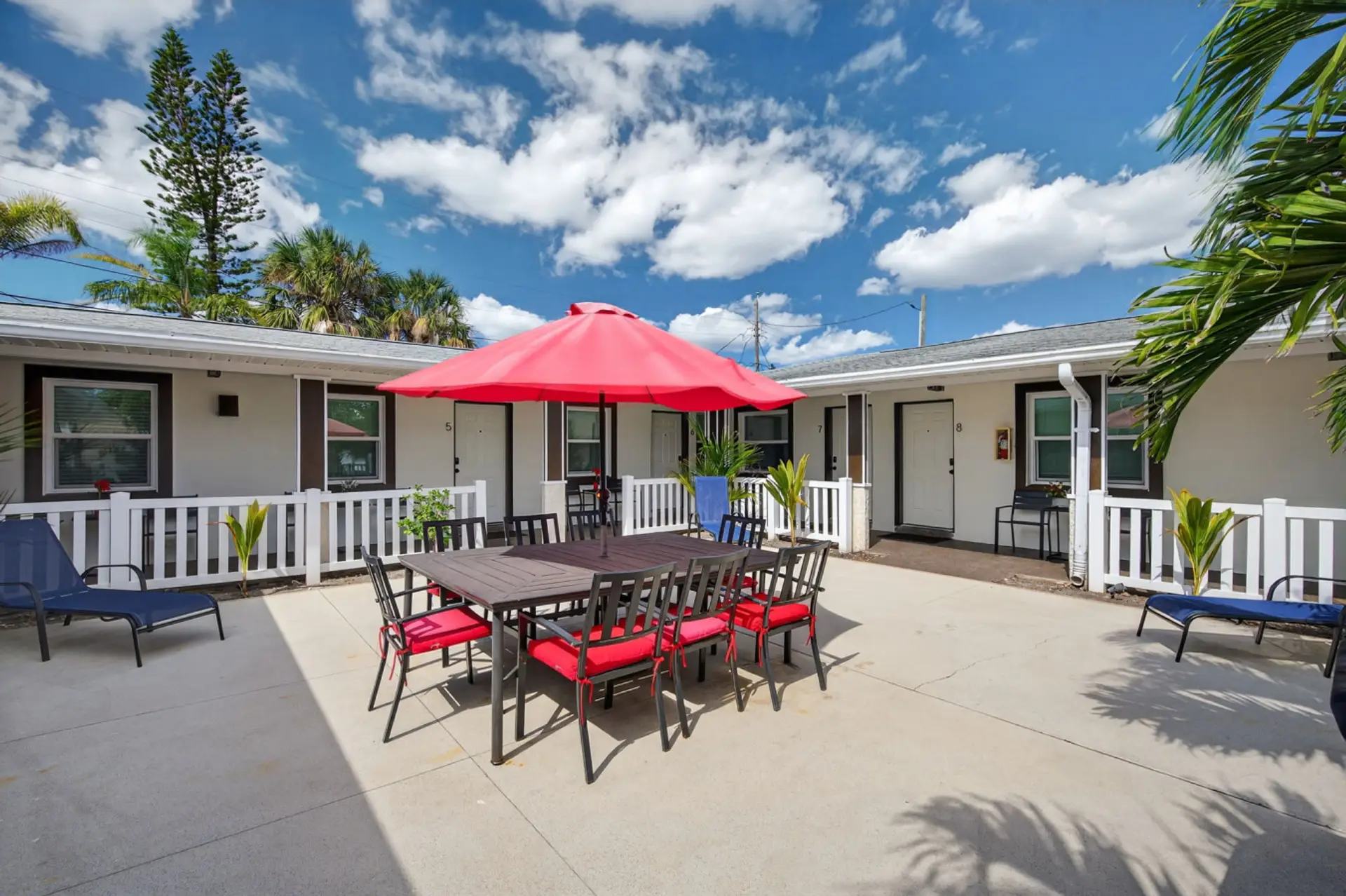 Sunny outdoor area w/ grill, dining table, & umbrellas for laid-back meals under blue skies.
