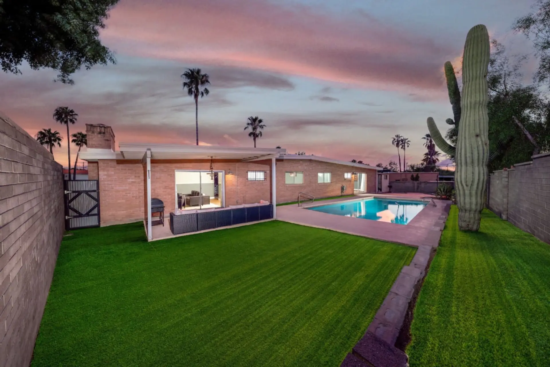 The whole backyard at golden hour — pool (unheated), grassy lawn, and a cozy patio with seating and grill