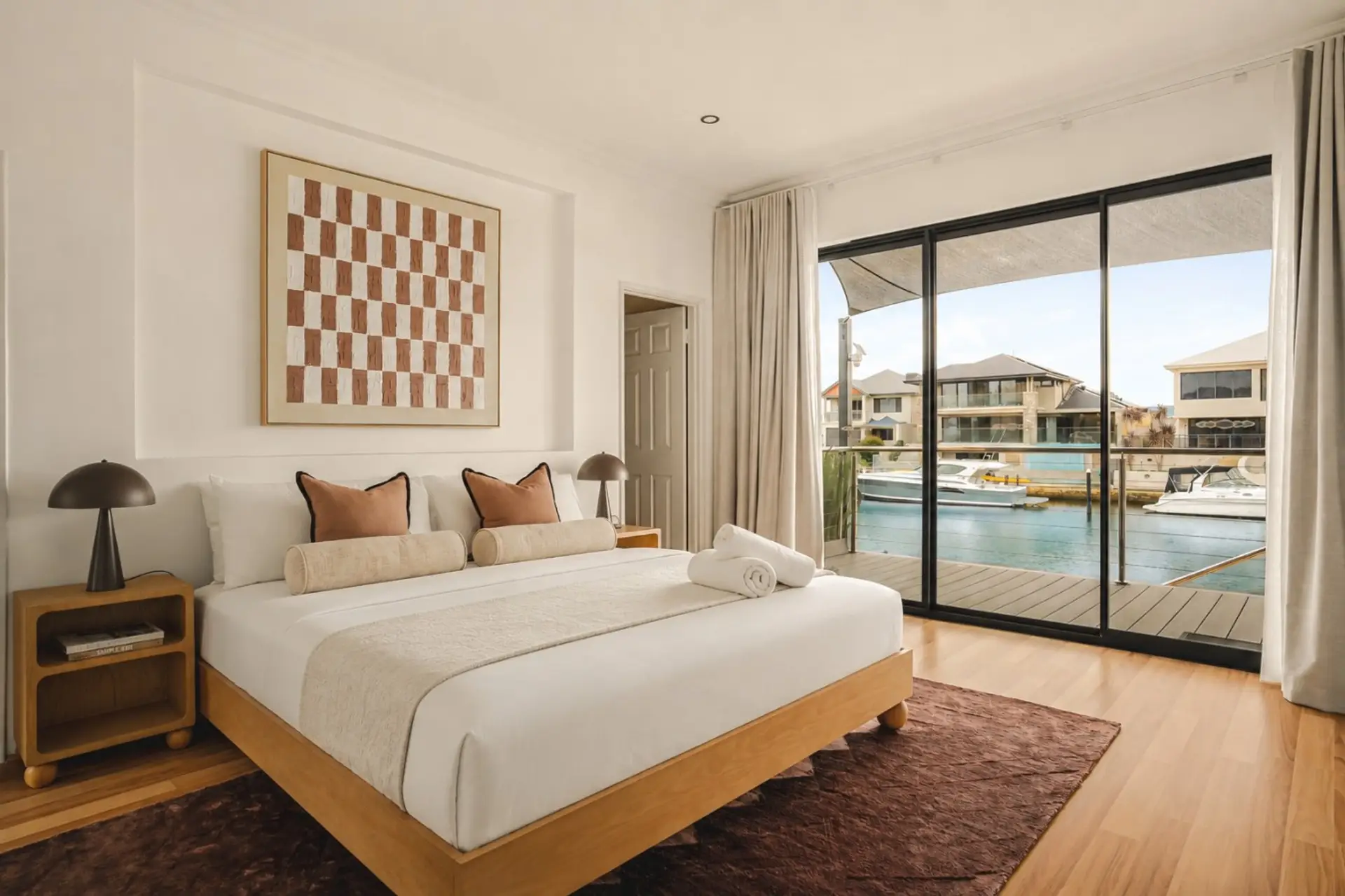 Luxury Halls Head canal-front bedroom with waterfront balcony access, quality linen, timber floors and stunning Mandurah waterway views.