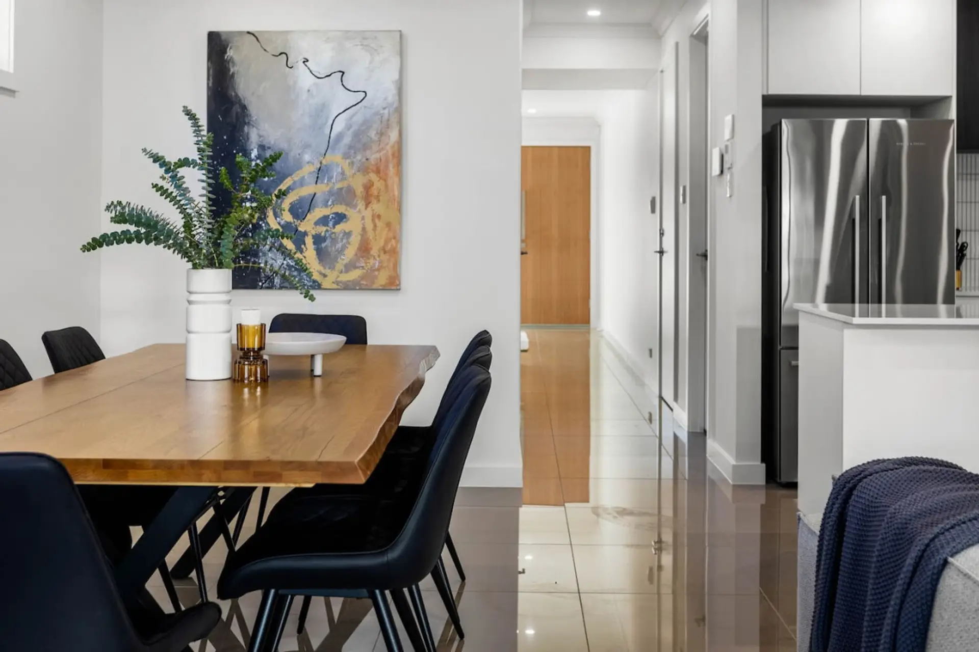 The scene extends to a sleek kitchen area with stainless steel appliances and a hallway leading to other rooms, creating a stylish and contemporary home environment.