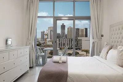 Main bedroom with a upholstered double bed, white dresser and large skyline window